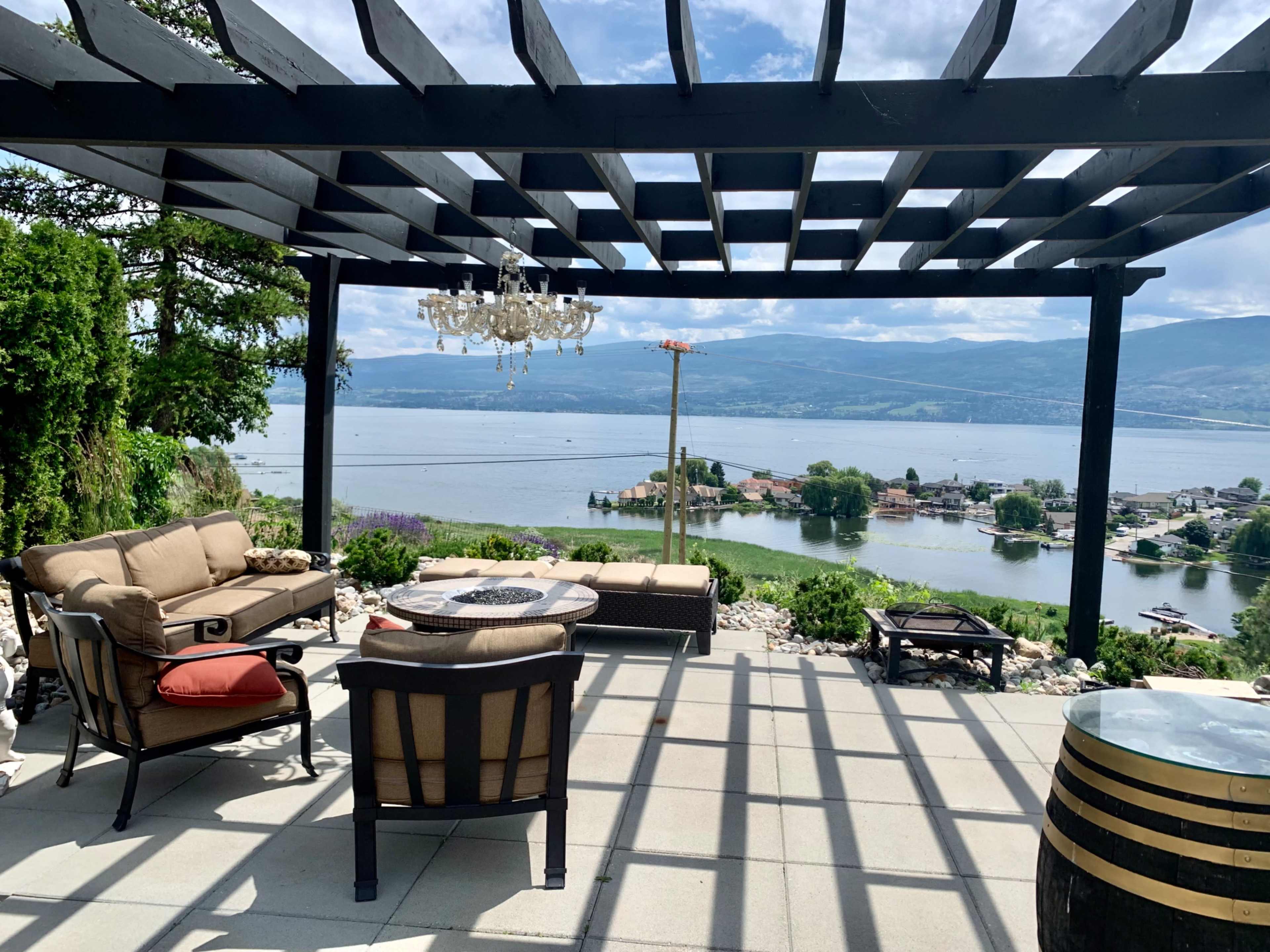 A patio with a pergola features outdoor seating and a view of a lake and distant hills.