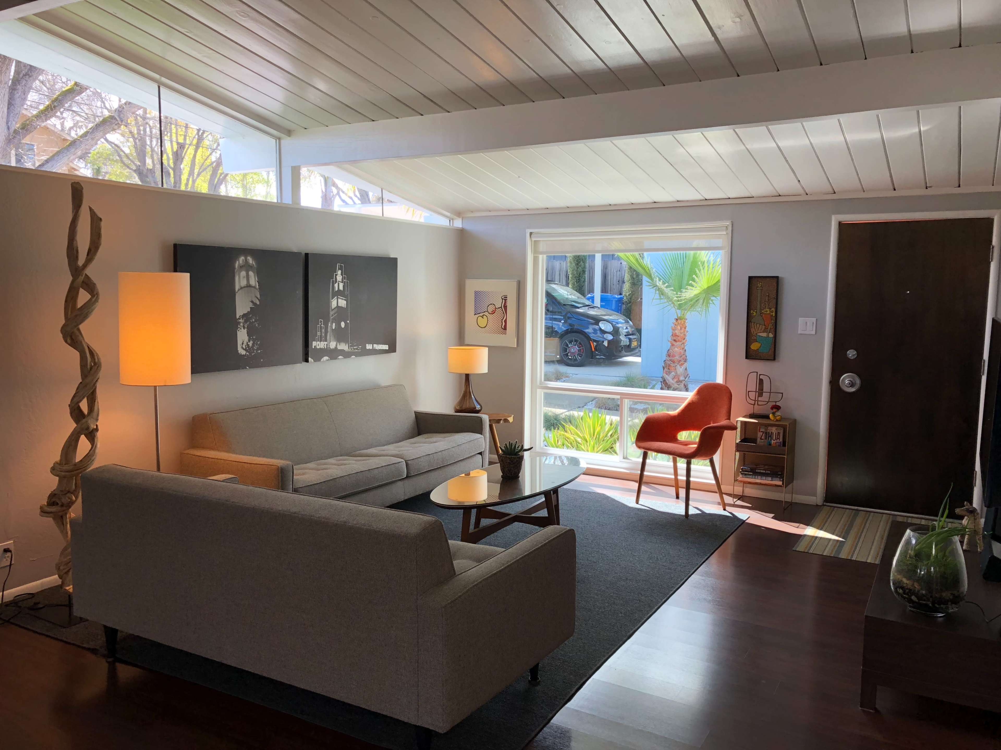 The image shows a modern living room with a gray sofa, a wooden coffee table, and a large window revealing a view of greenery outside.