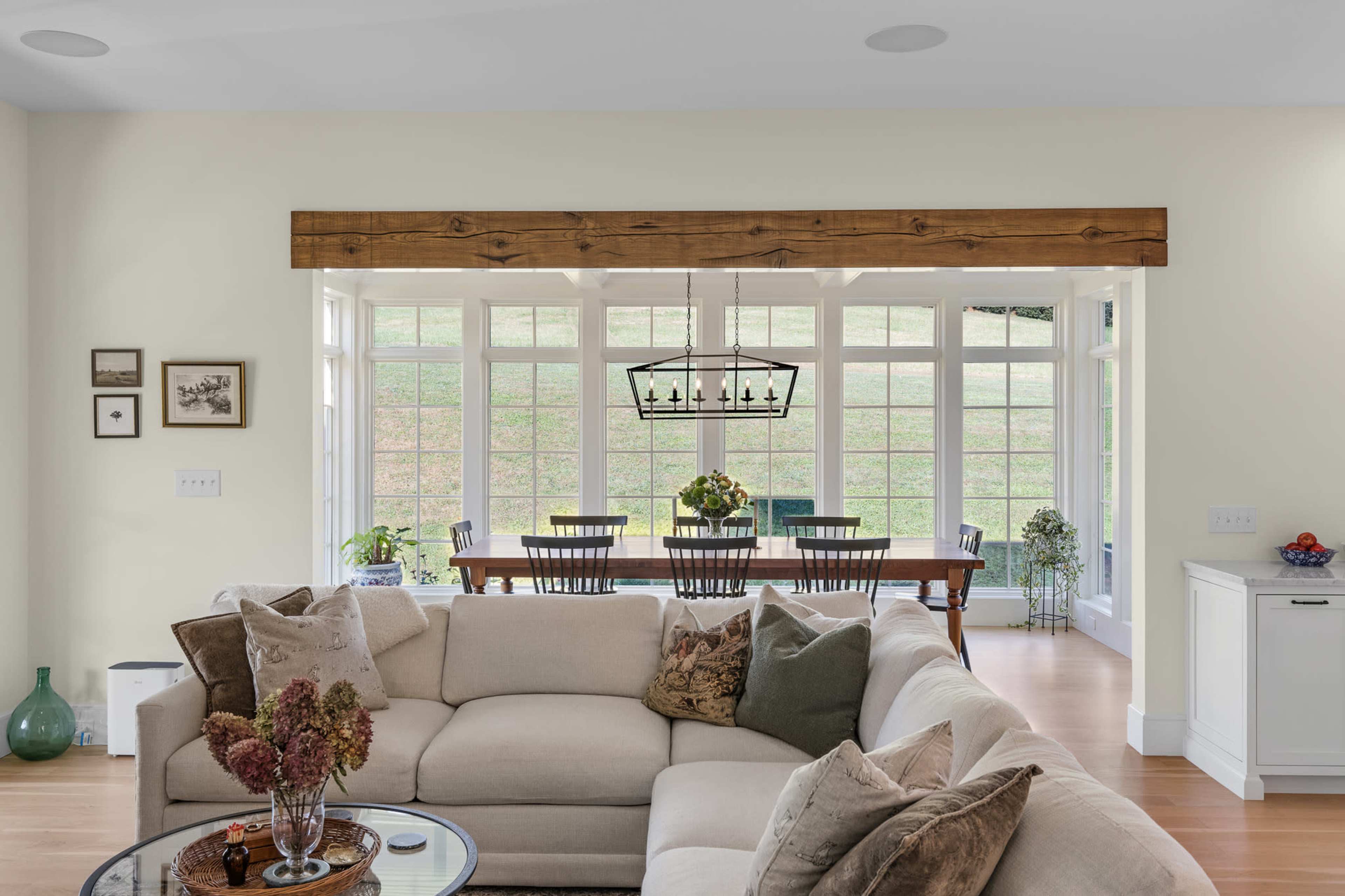 A spacious living room features a large L-shaped sectional sofa and a dining area with a table and chairs visible through large windows.
