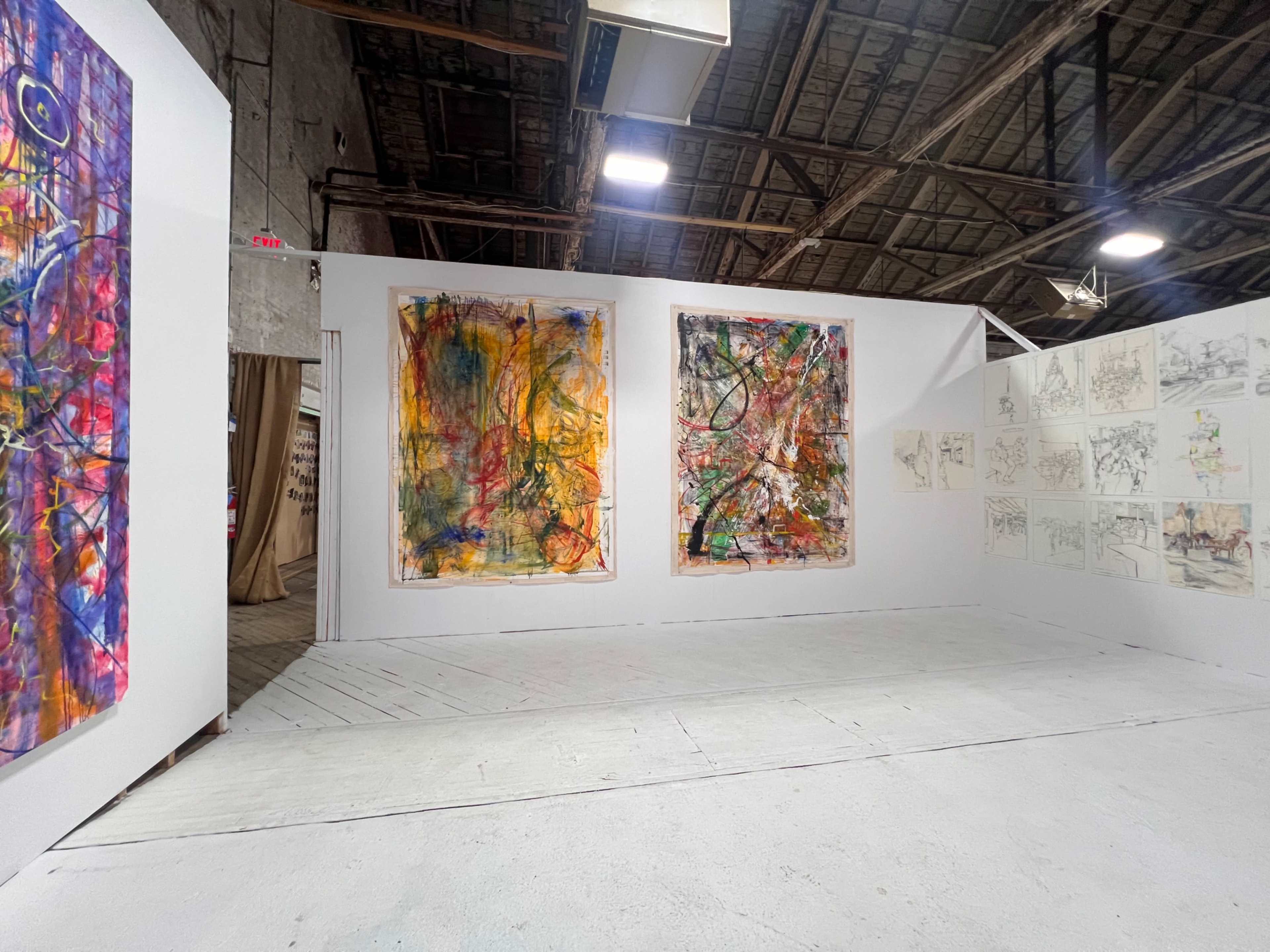 An art exhibition space featuring three large abstract paintings hung on white walls, with sketches displayed on the adjacent wall and a wooden floor beneath.