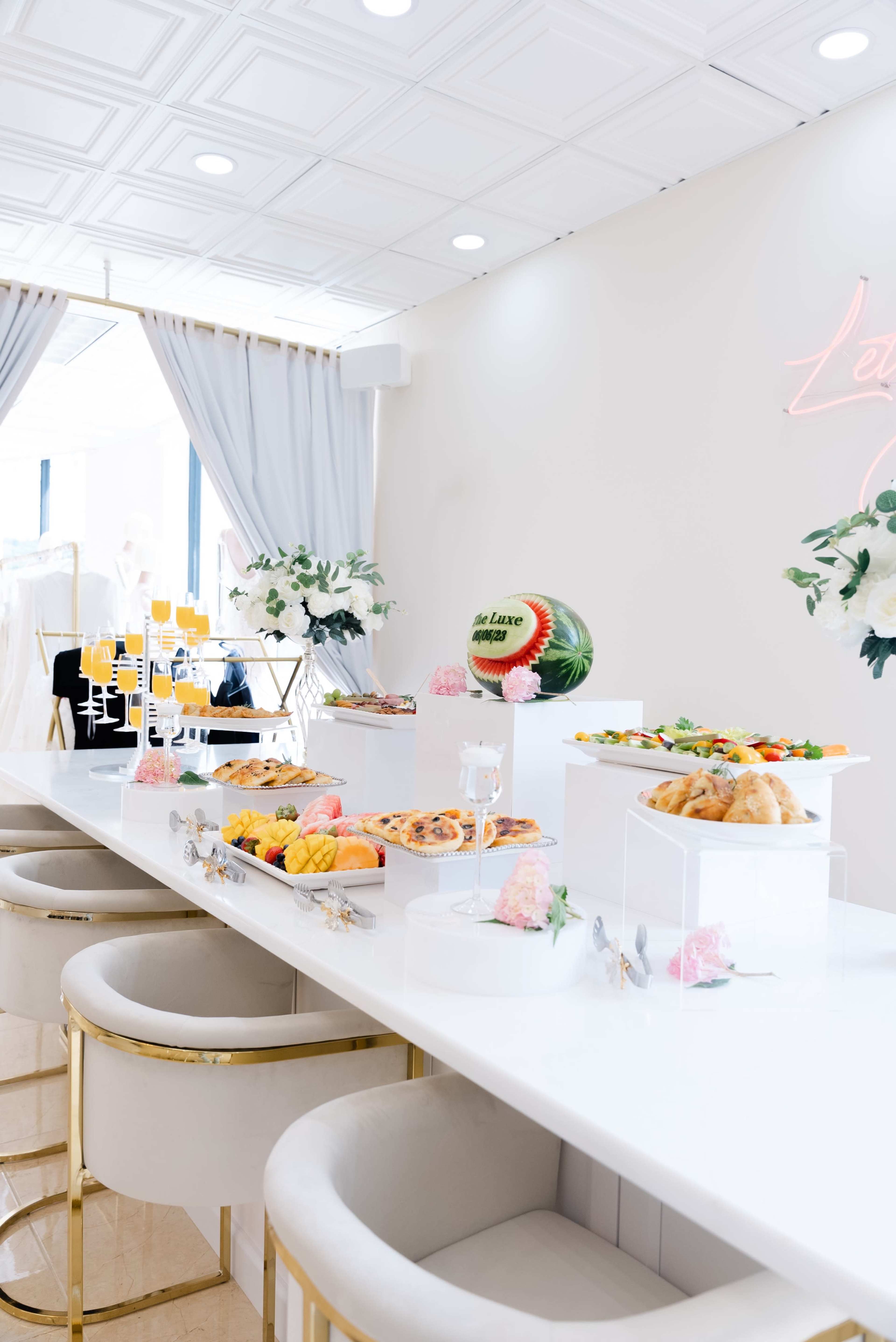 A bright, elegant table featuring an array of colorful dishes and refreshments, including pastries, fruit, and decorative floral touches.