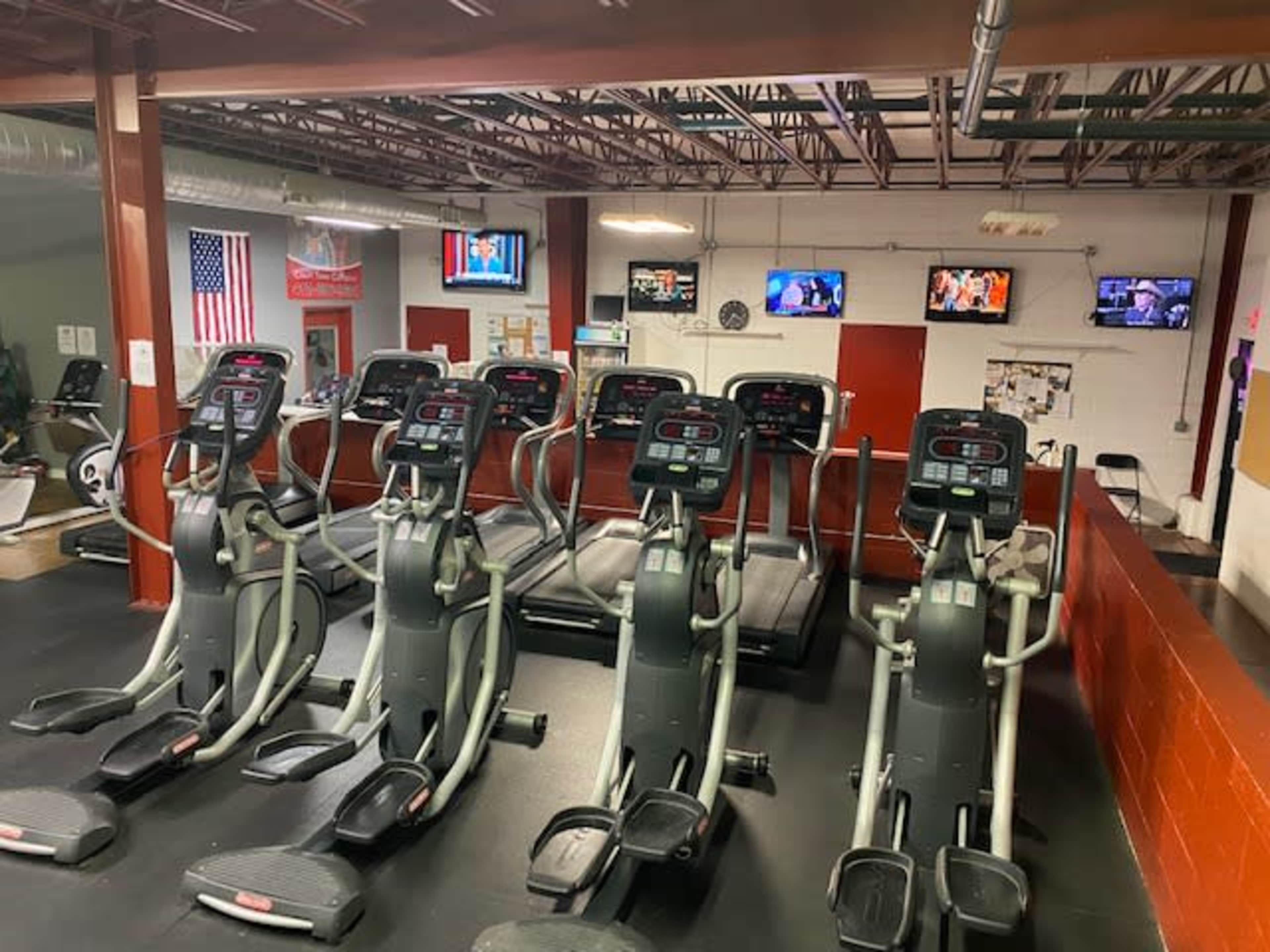 A gym with several elliptical machines arranged in a row, with multiple televisions mounted on the walls.