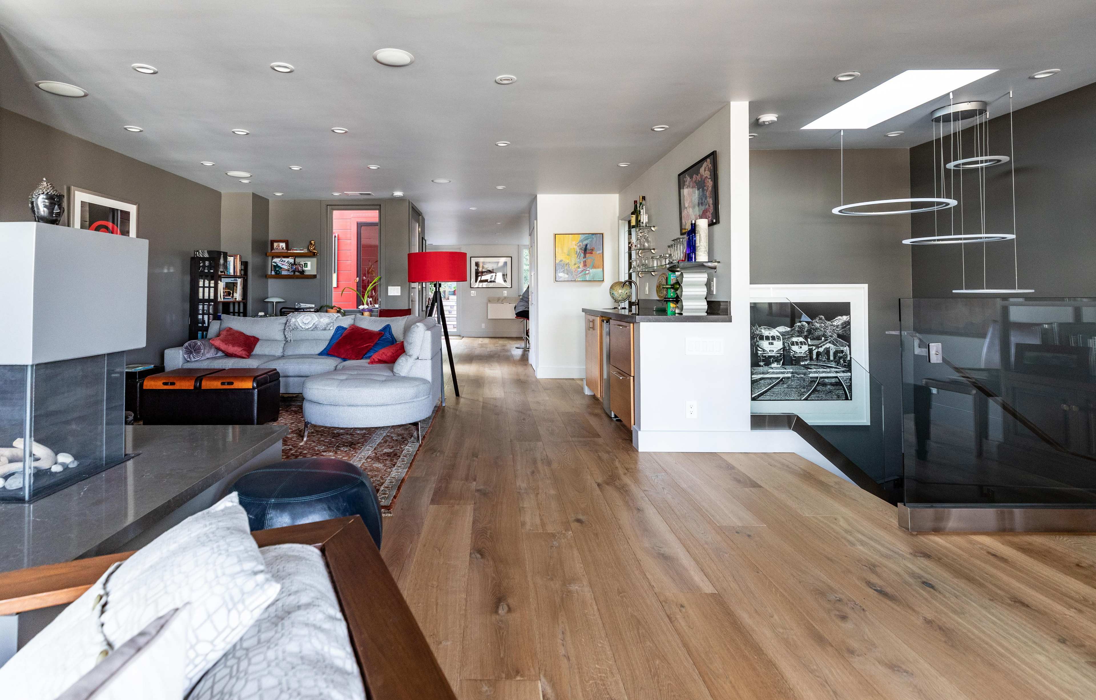 A modern interior space featuring an open living area with a blue sectional couch, a dining area, a kitchenette, and a staircase leading to a lower level.