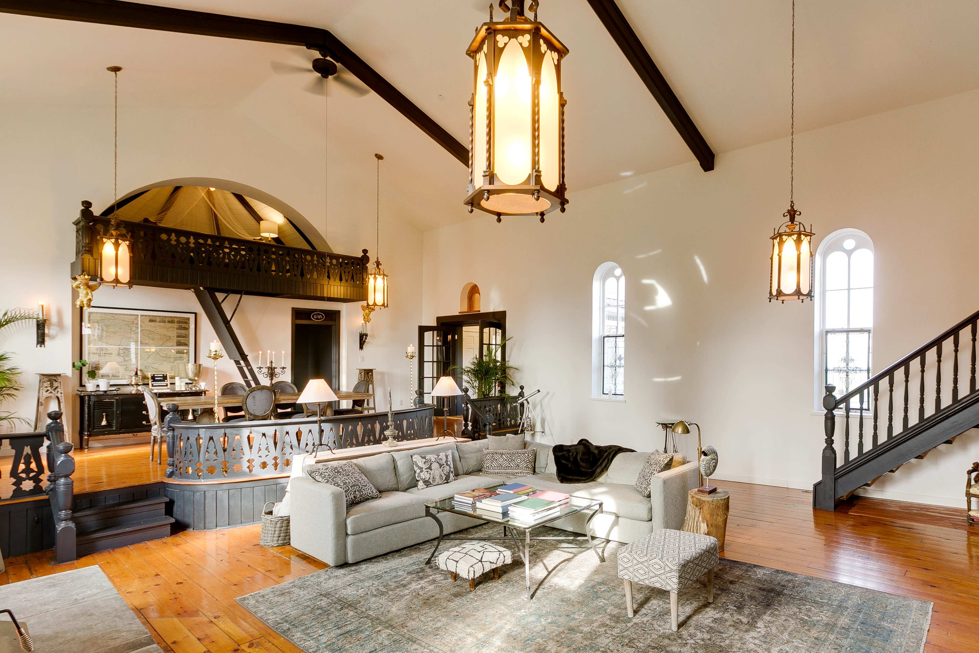 The image features a spacious living area with high ceilings, large windows, and a mix of modern furnishings and architectural details.