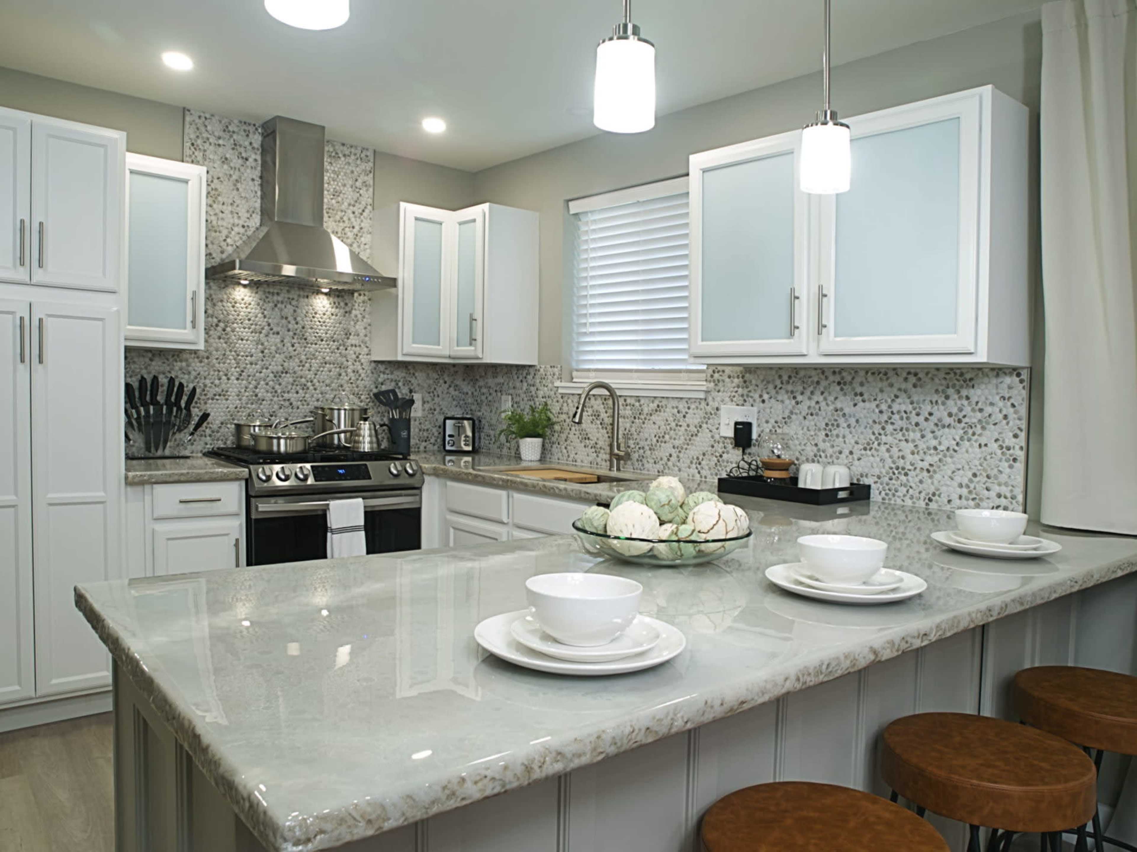 A modern kitchen with white cabinets, a gray countertop, and pendant lighting above a central island.