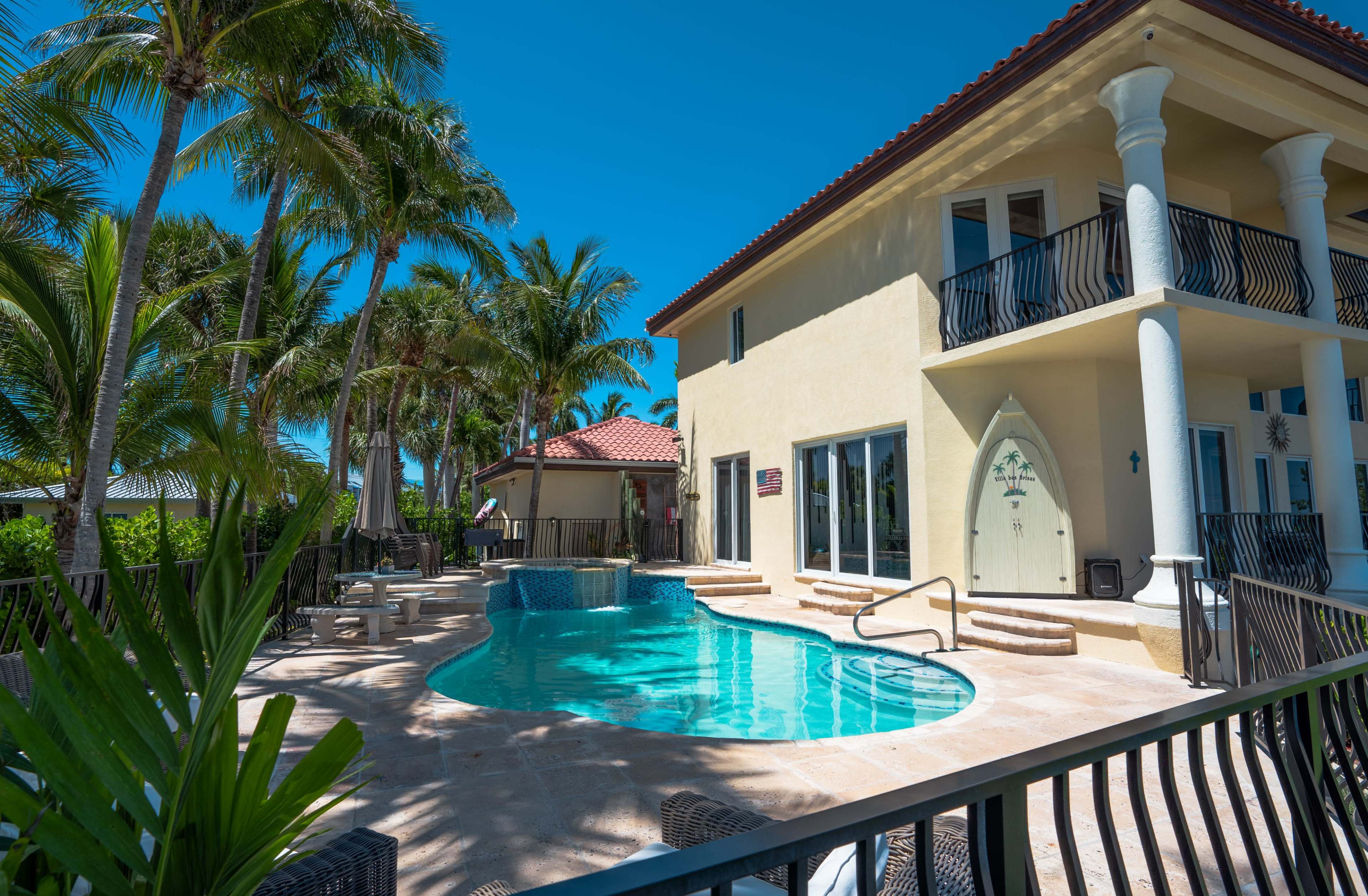 A luxurious home features a swimming pool surrounded by palm trees and outdoor seating areas.