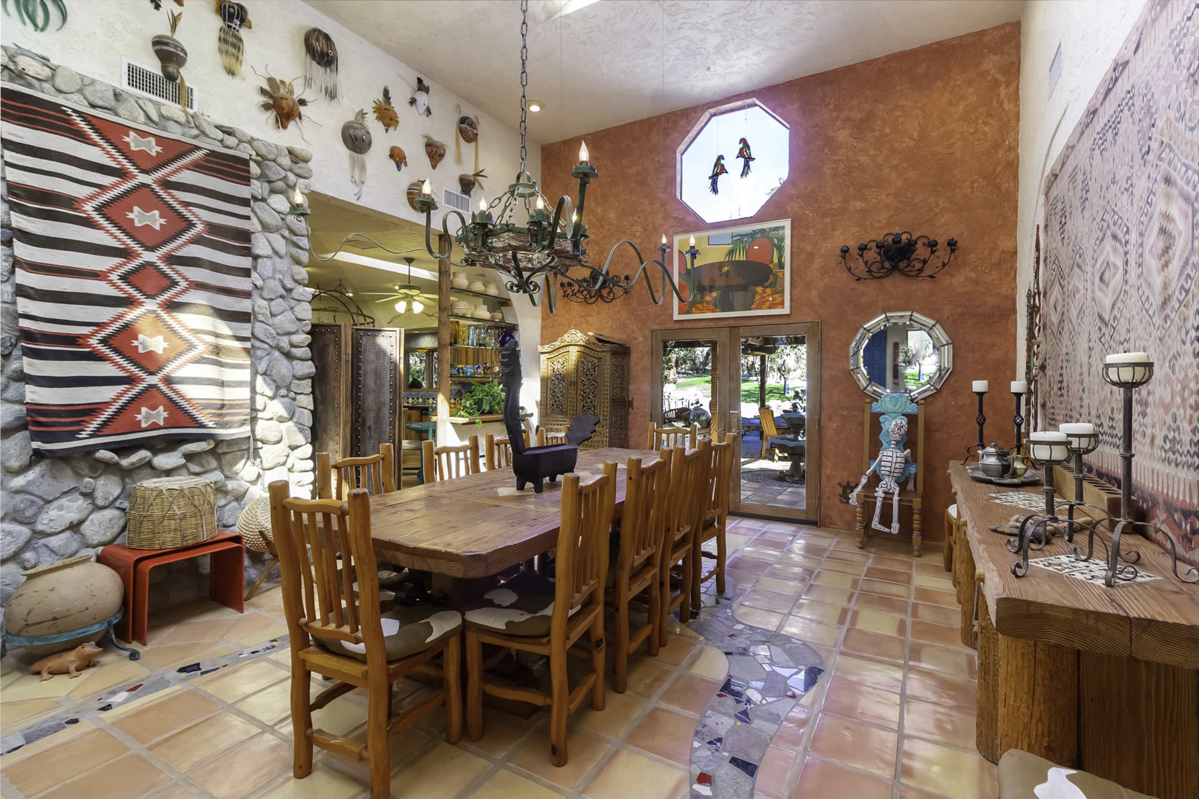 A spacious dining area featuring a large wooden table surrounded by chairs, with decorative wall hangings and a stone wall.