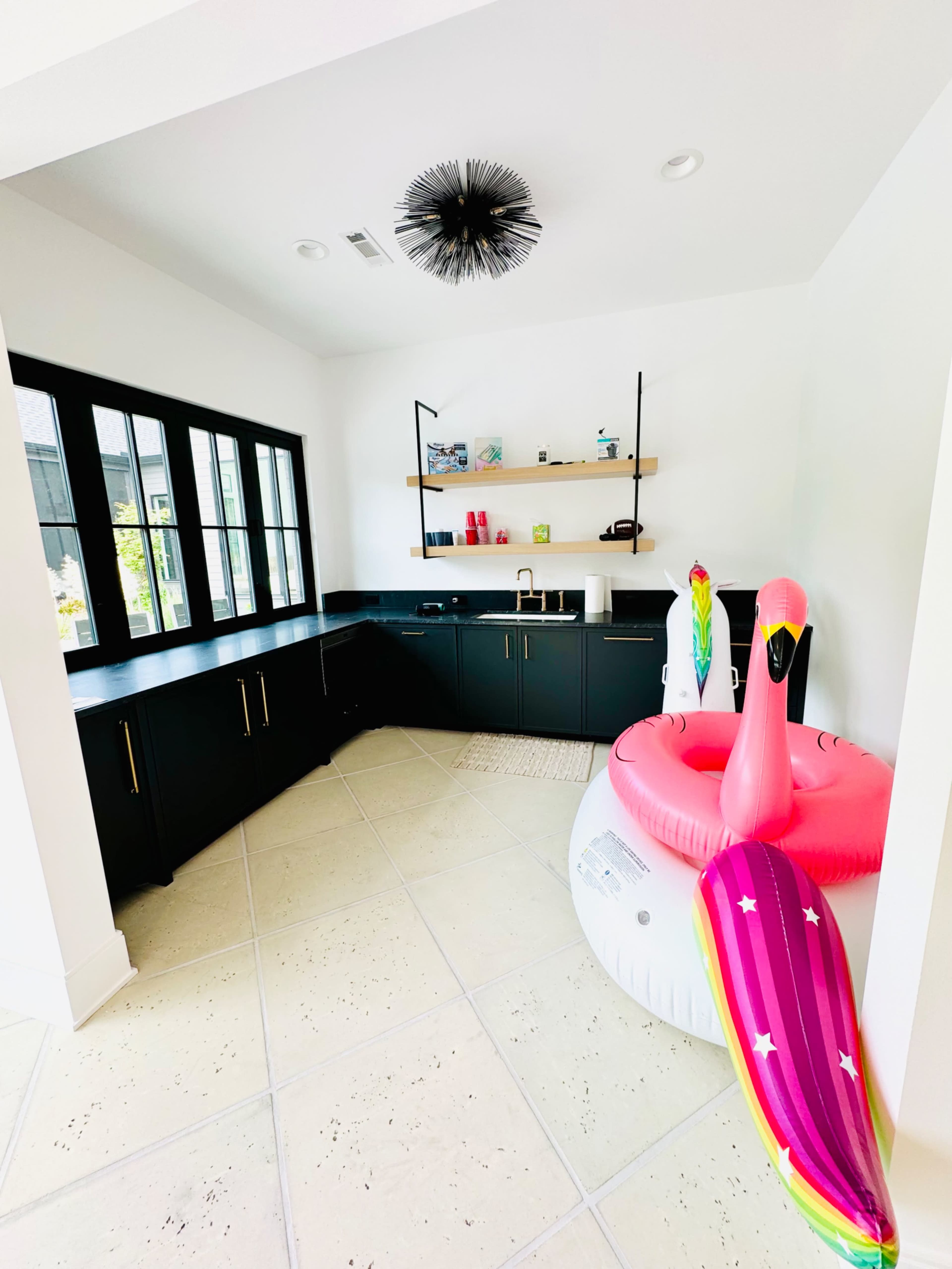 A modern room with black cabinetry, a decorative light fixture, and a large inflatable flamingo and a pool float.
