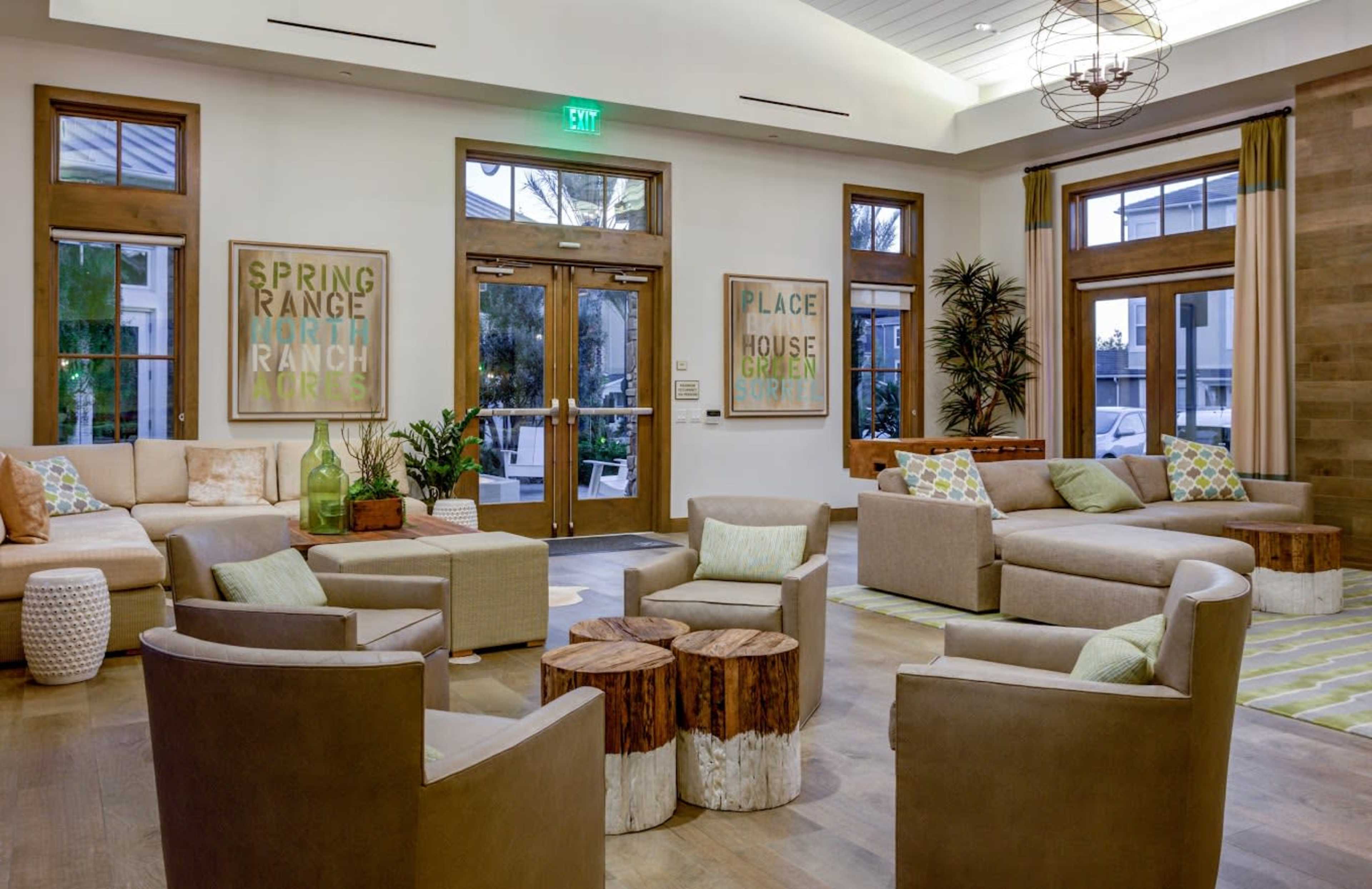 A modern lobby features comfortable seating arrangements, wooden tables, and large framed artworks on the walls.