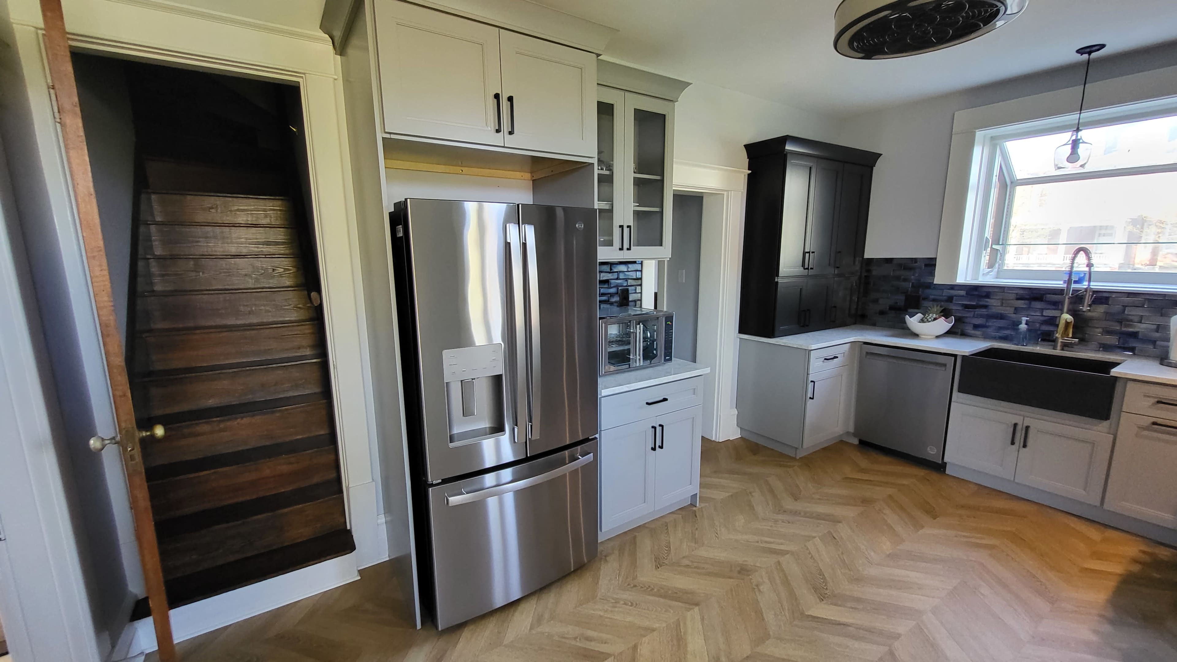 A modern kitchen featuring a stainless steel refrigerator, a farmhouse sink, and a staircase leading to an upper level.