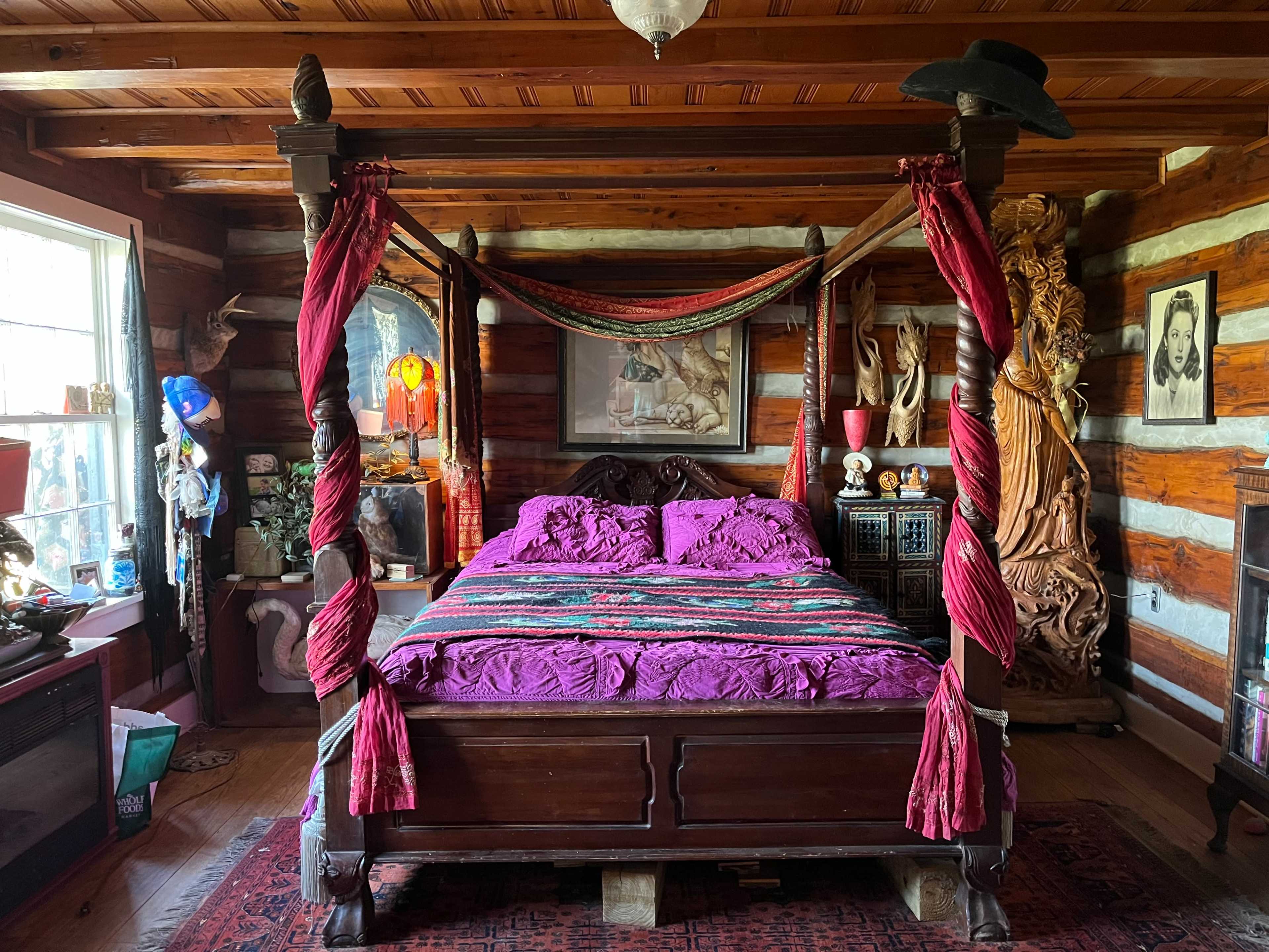 A cozy log cabin bedroom featuring a four-poster bed draped in colorful fabric, surrounded by rustic wooden decor and various decorative items.
