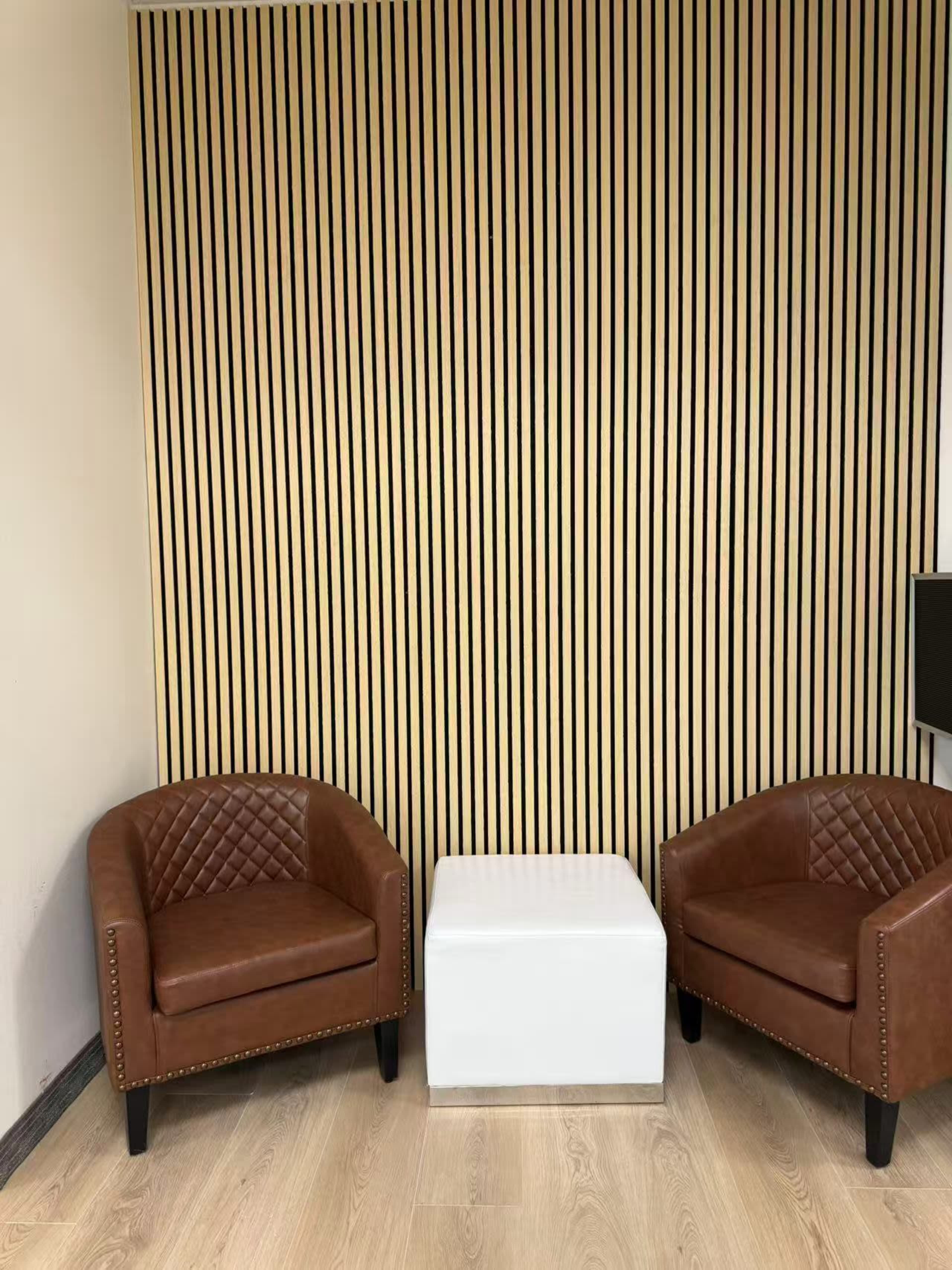 The image shows two brown leather armchairs and a white coffee table set against a vertical striped wooden wall.