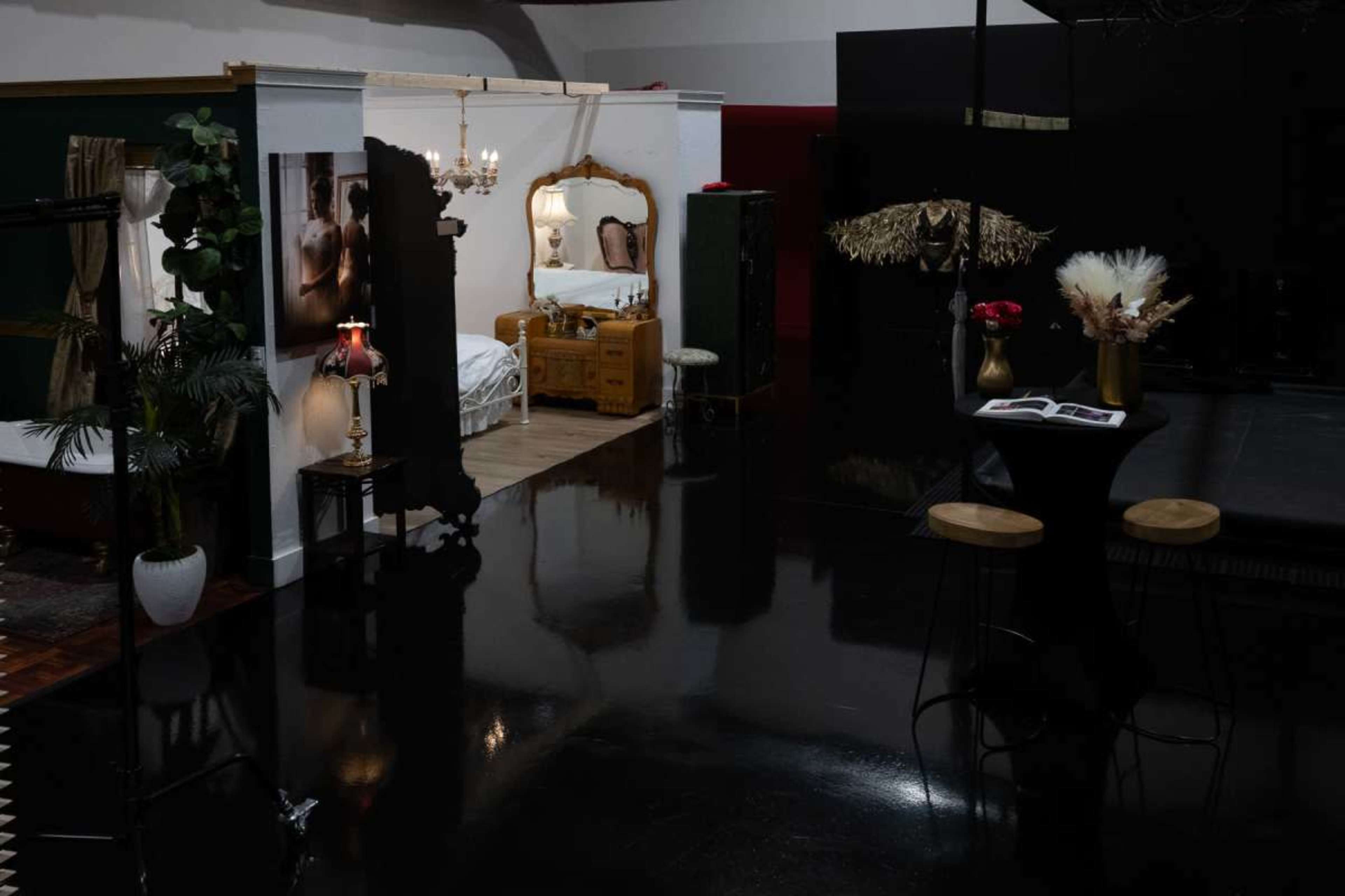 The image shows a spacious interior with a stylish bedroom area featuring a vintage bed and decorative elements, alongside a small dining setup with two stools and a table.