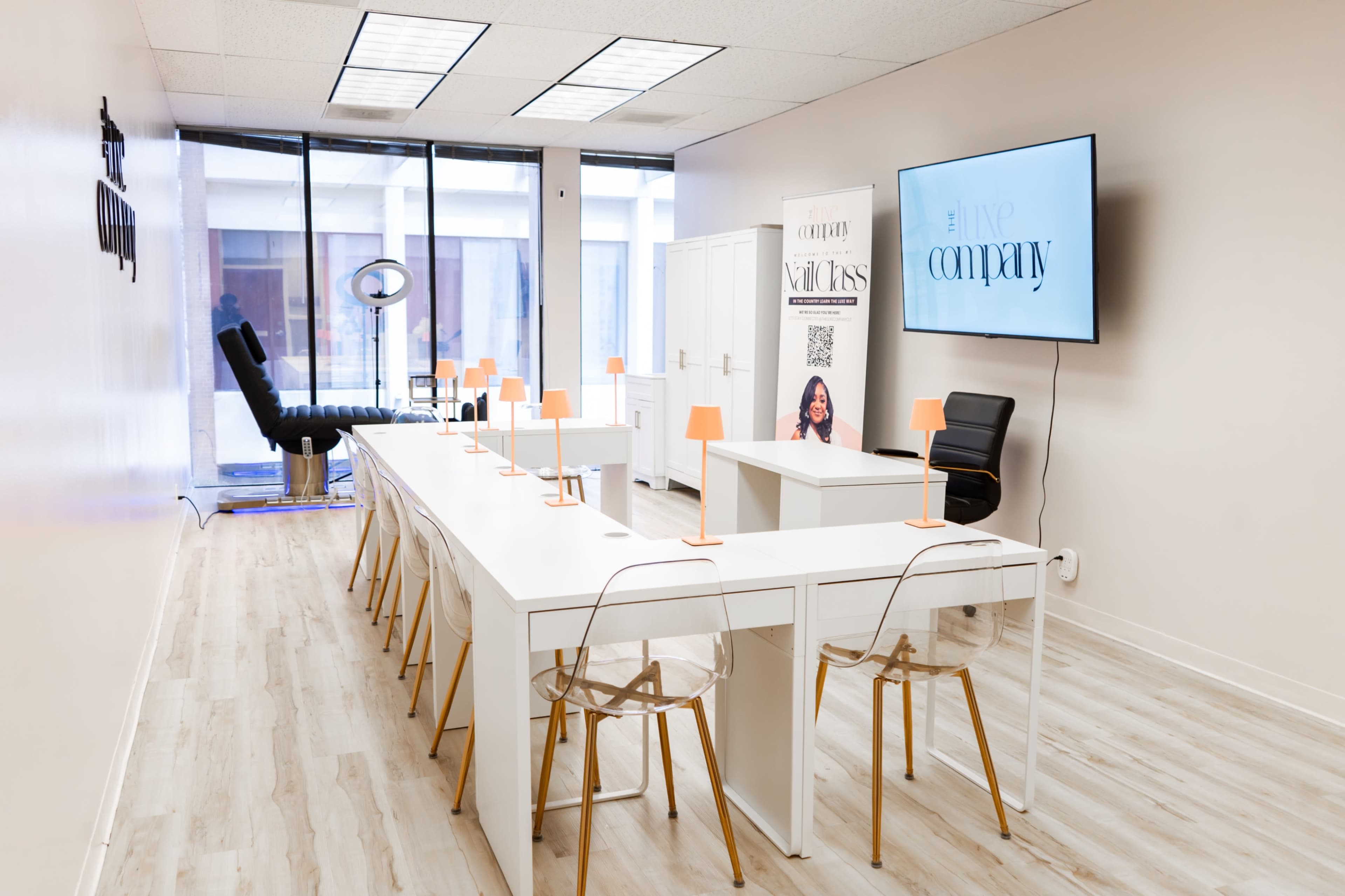 The image shows a modern office space with a long white table, clear acrylic chairs, and a large screen on the wall, featuring a banner for a company.
