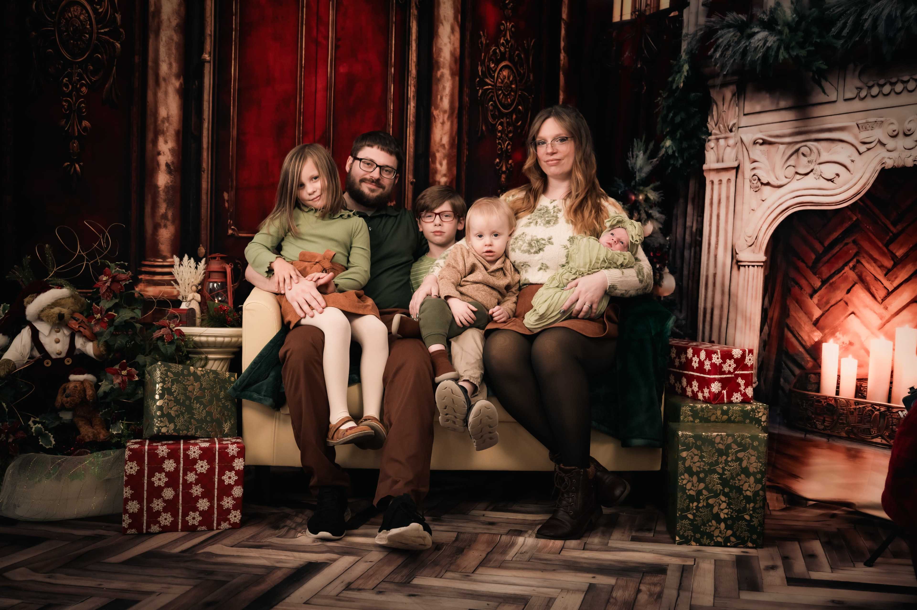 A family of five poses for a holiday portrait on a couch, surrounded by festive decorations and gifts.