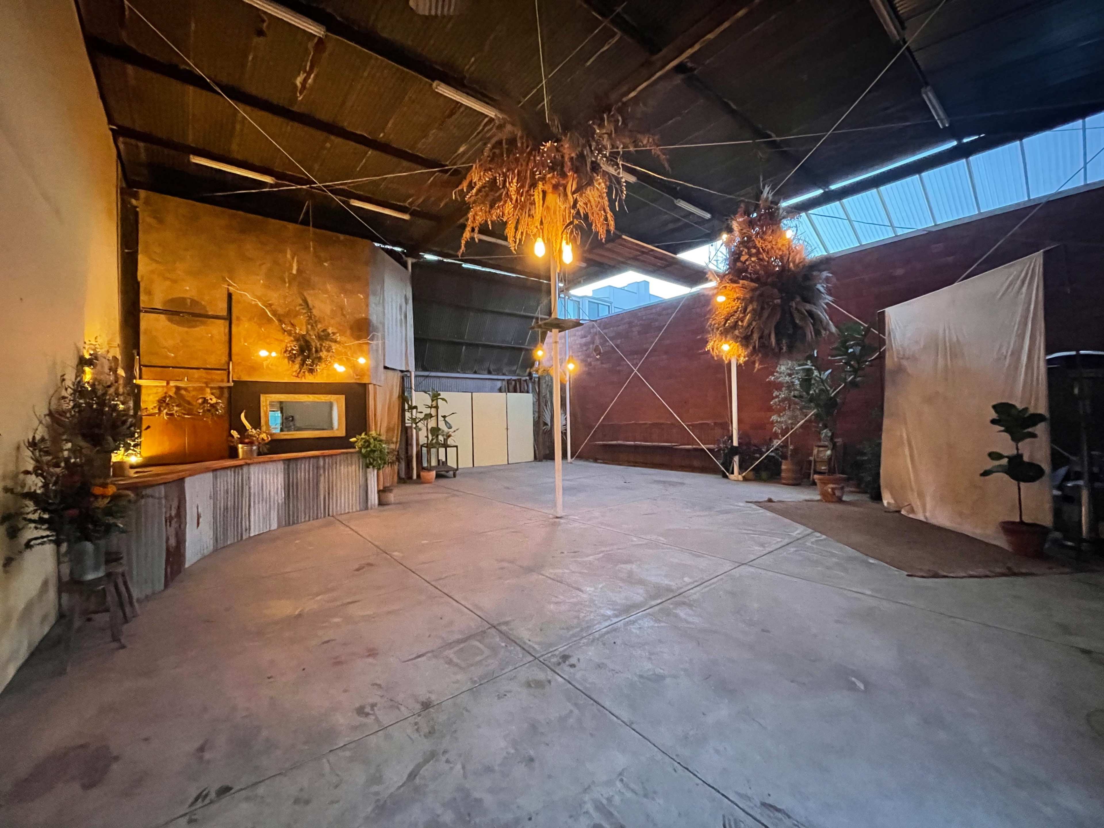 The image shows an empty industrial-style space with a wooden counter, hanging plants, and decorative lights.