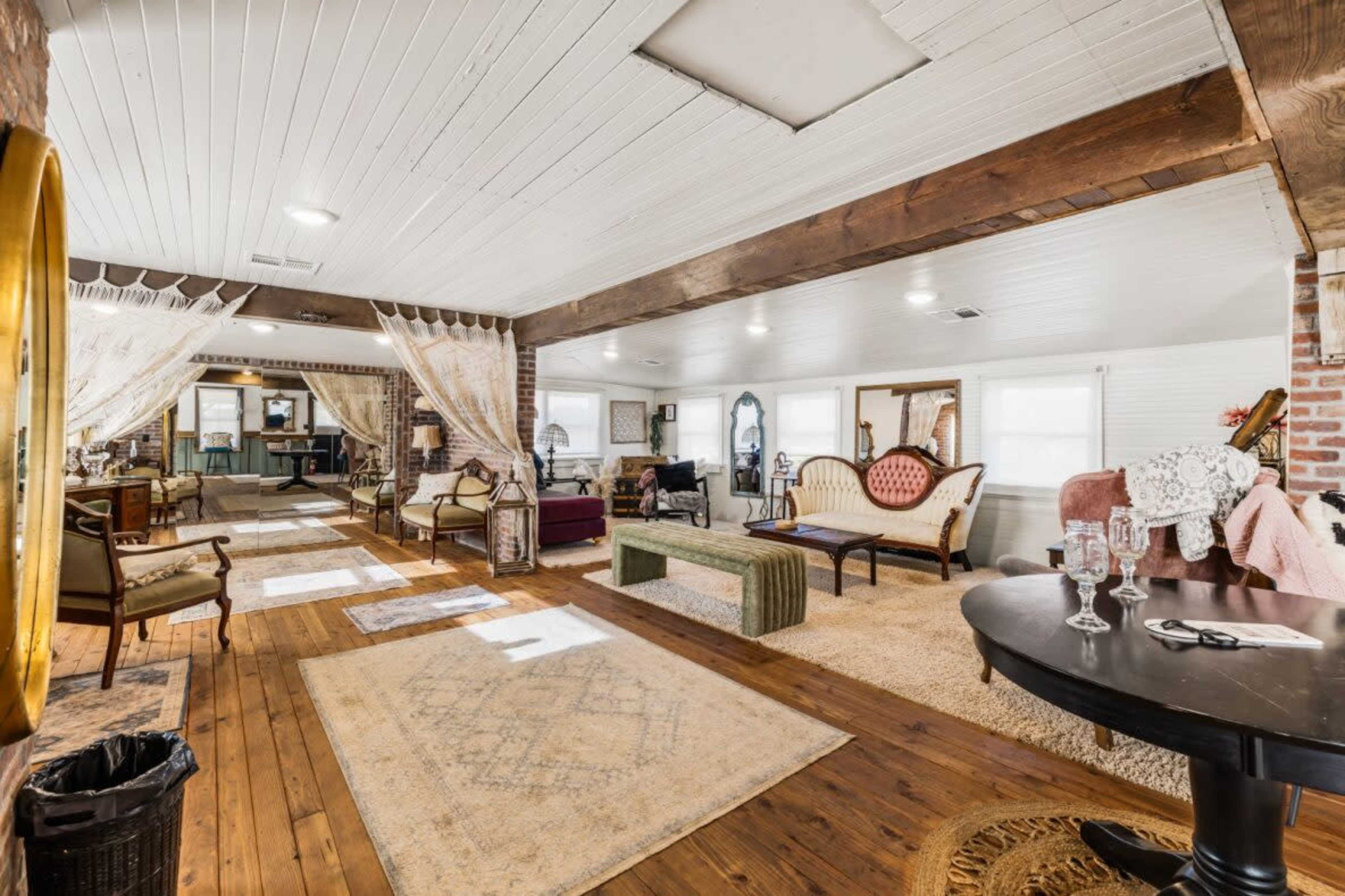 The spacious interior features a living area with wooden floors, various seating arrangements, and large windows allowing natural light.