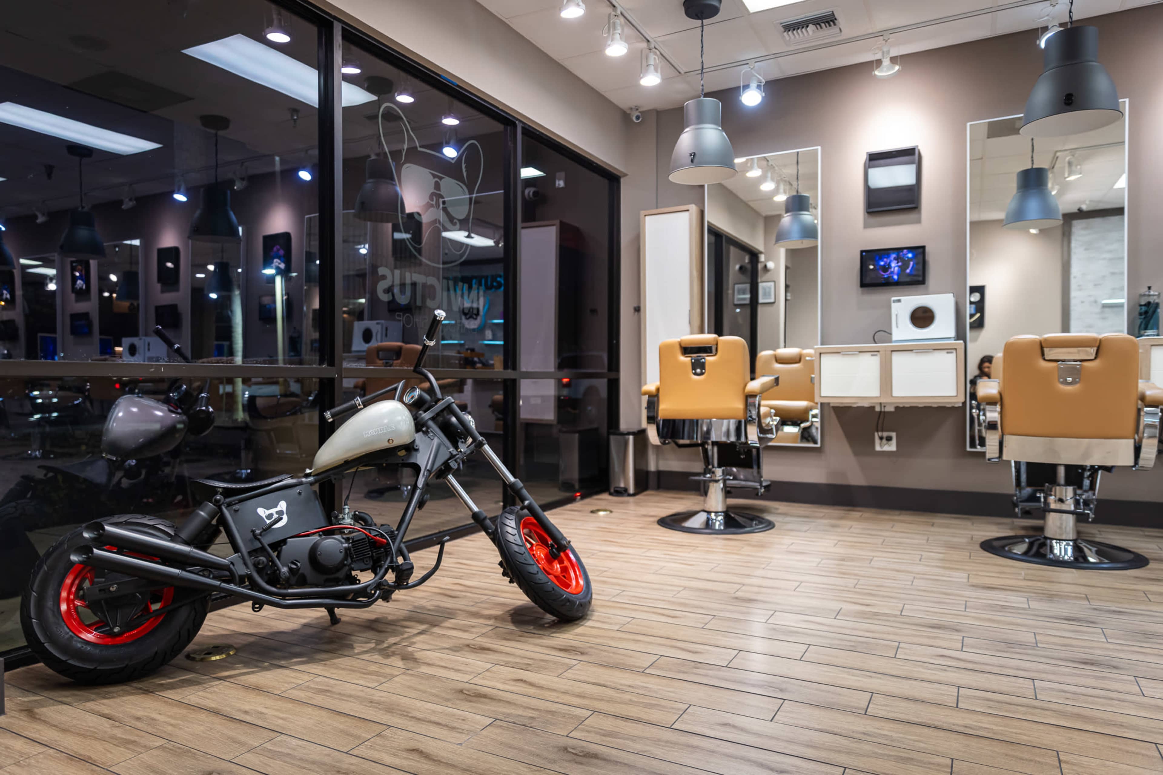 The image shows a salon interior featuring two barber chairs, large mirrors, and a motorcycle parked on the wooden floor.