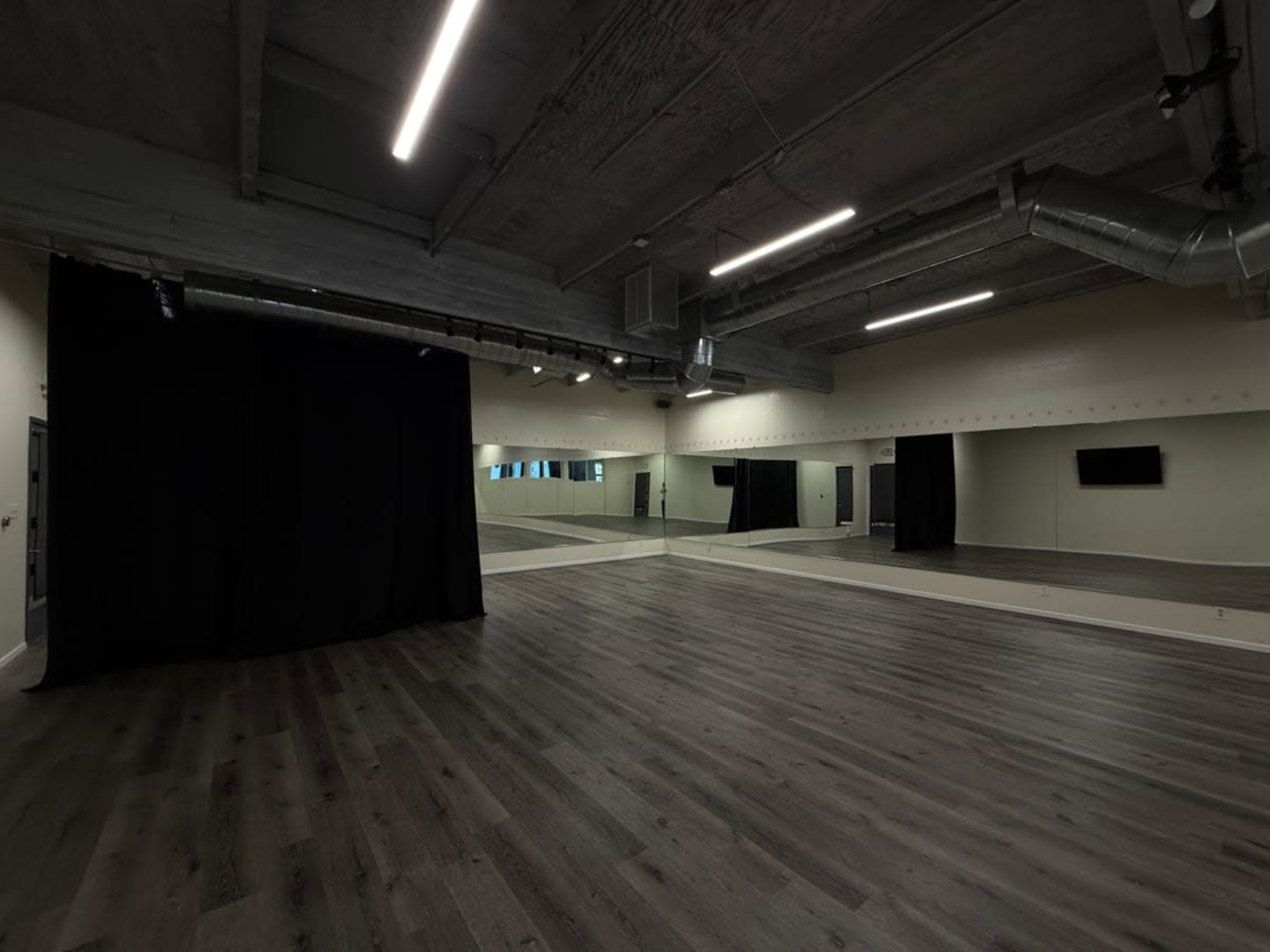 The image shows a spacious, empty dance studio with mirrored walls, wooden flooring, and a black curtain on one side.