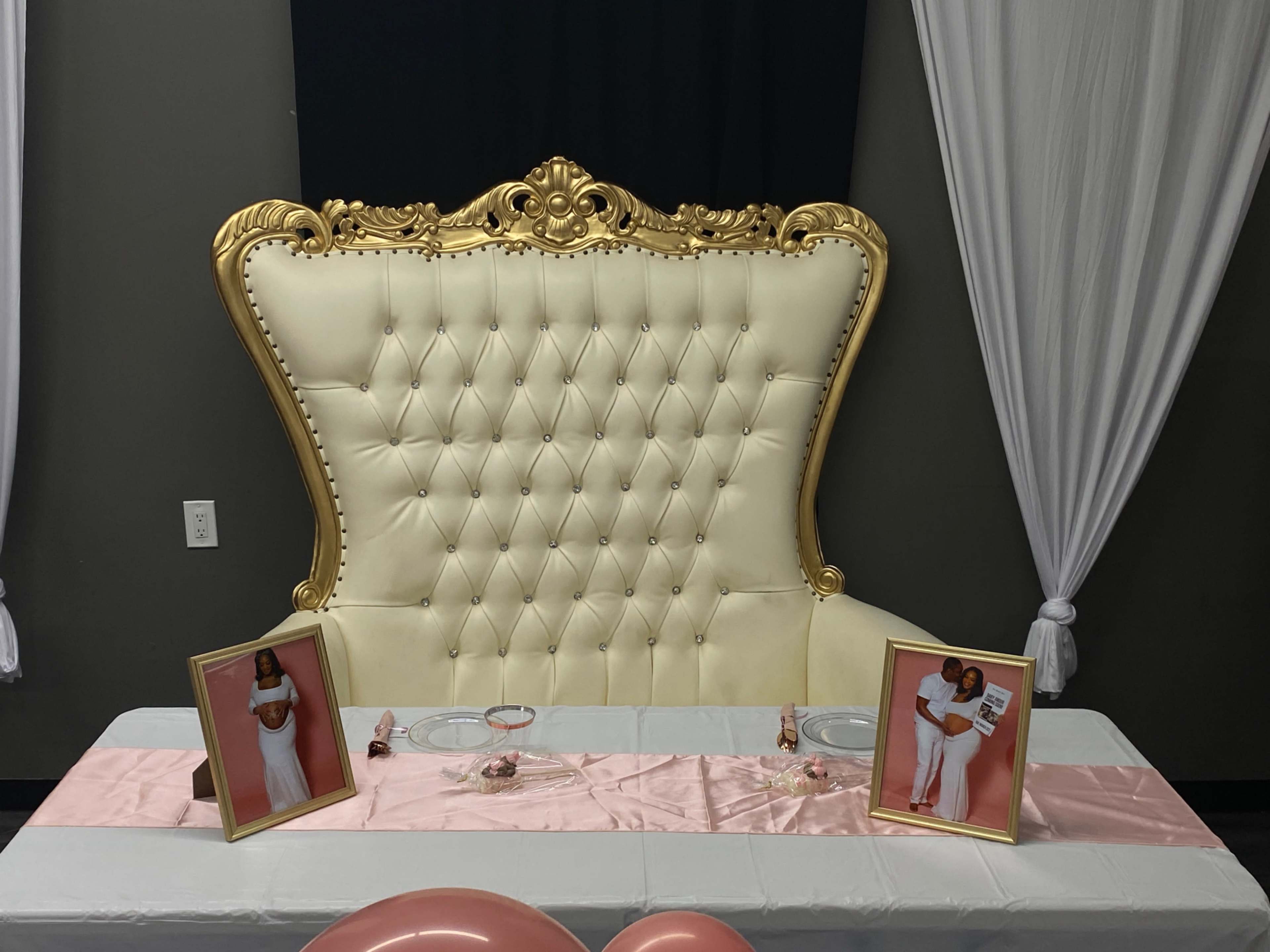 The image shows a lavish, gold-accented tufted throne chair at a decorated table with two framed photos on either side.