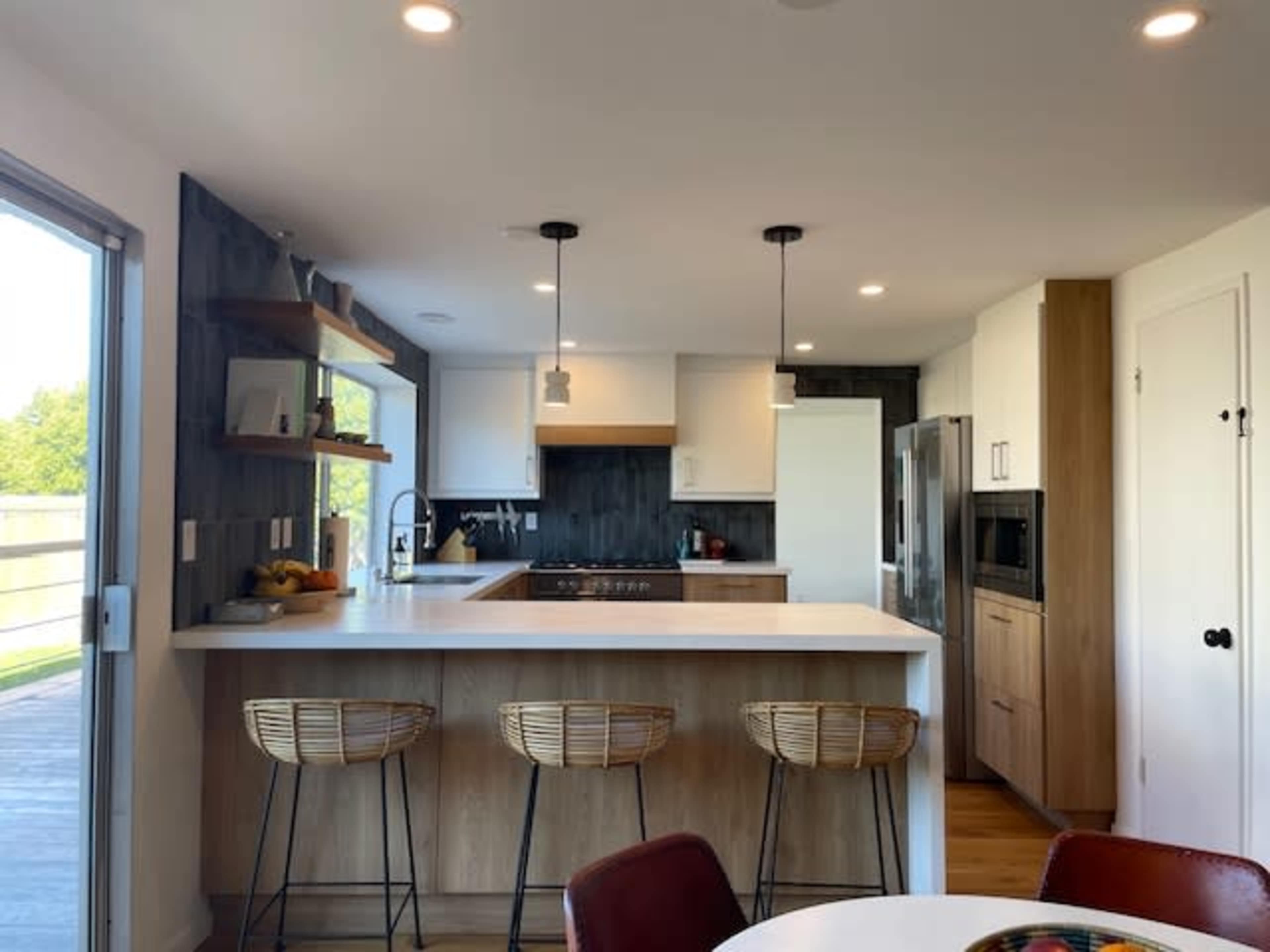 A modern kitchen features a central island with bar stools, white countertops, and a mix of wood and white cabinetry.