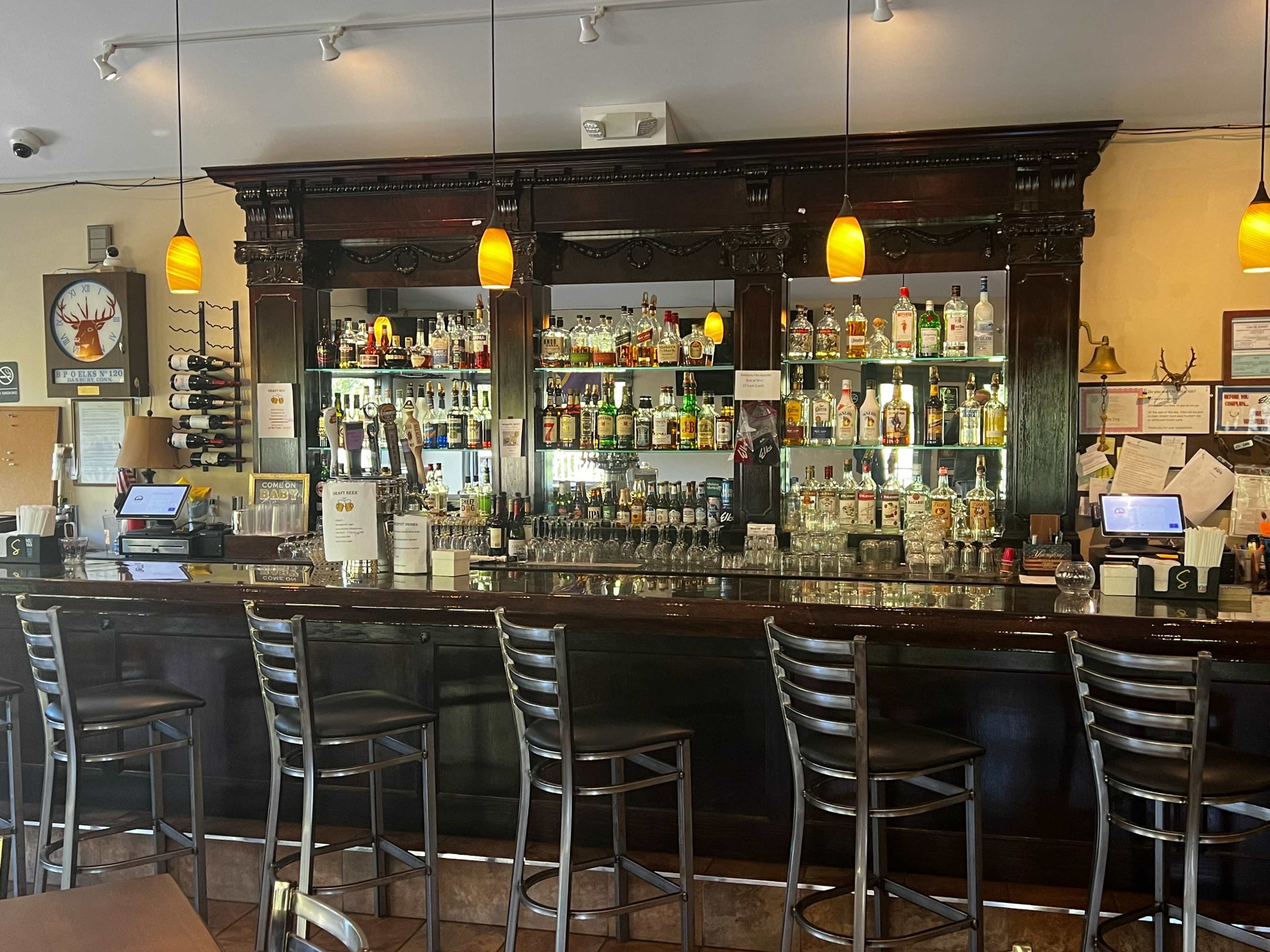 A well-lit bar with shelves stocked with various liquor bottles, surrounded by high stools.