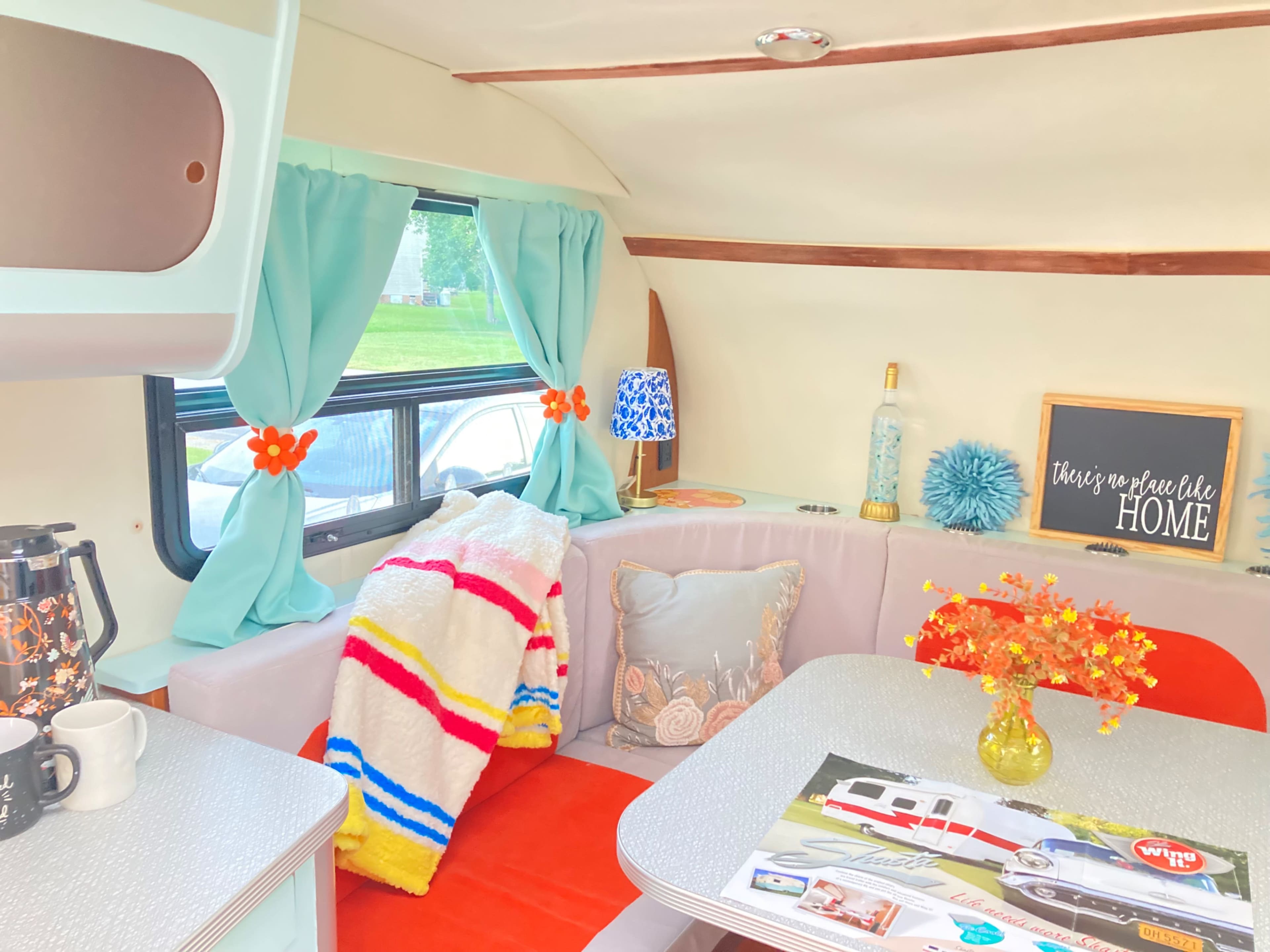 The interior of a retro camper features a cozy seating area with colorful throw pillows, a small table, and decorative items.