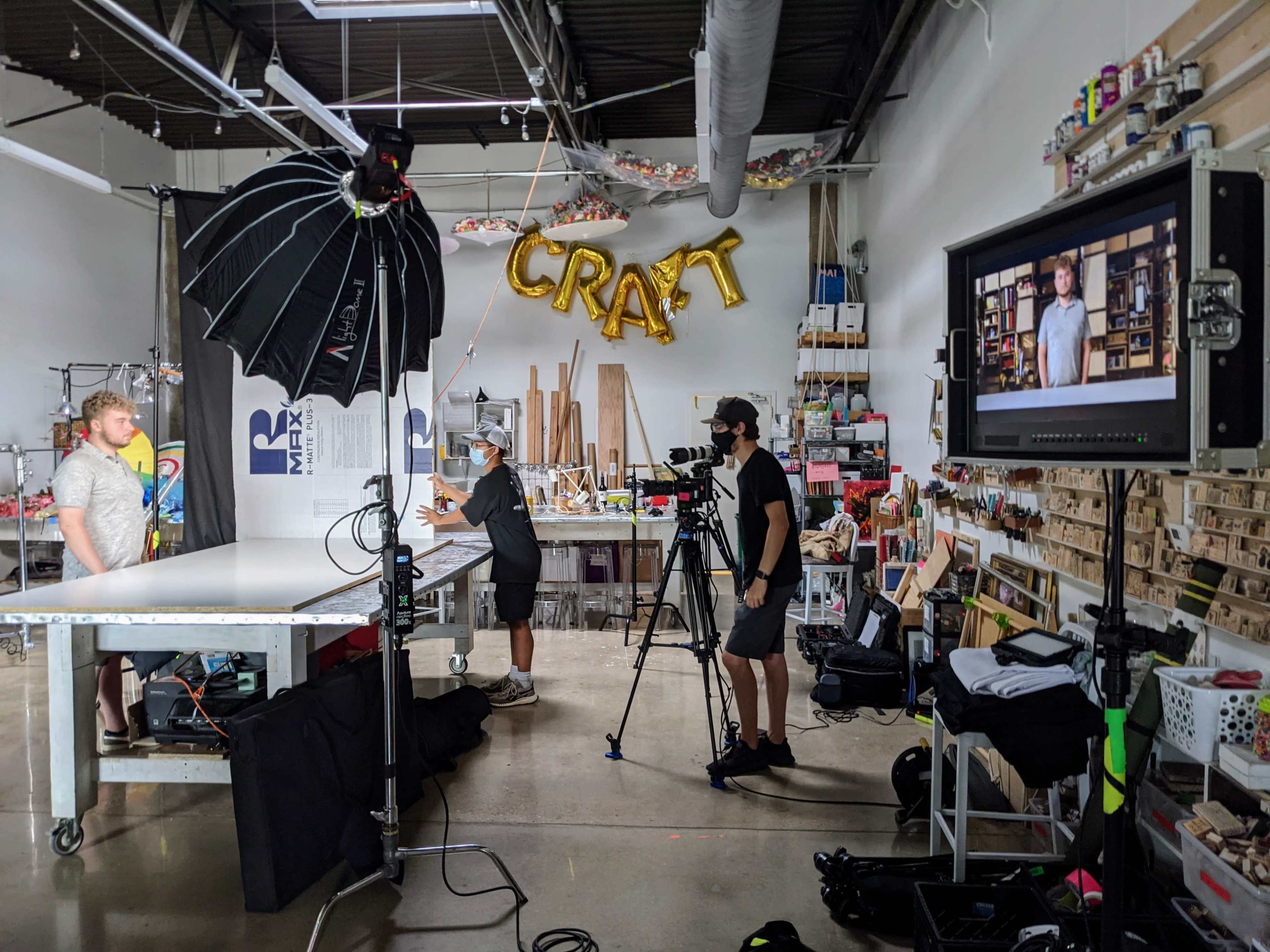 A photography studio is set up with a large backdrop and bright lights, featuring two people interacting while a camera records the scene.