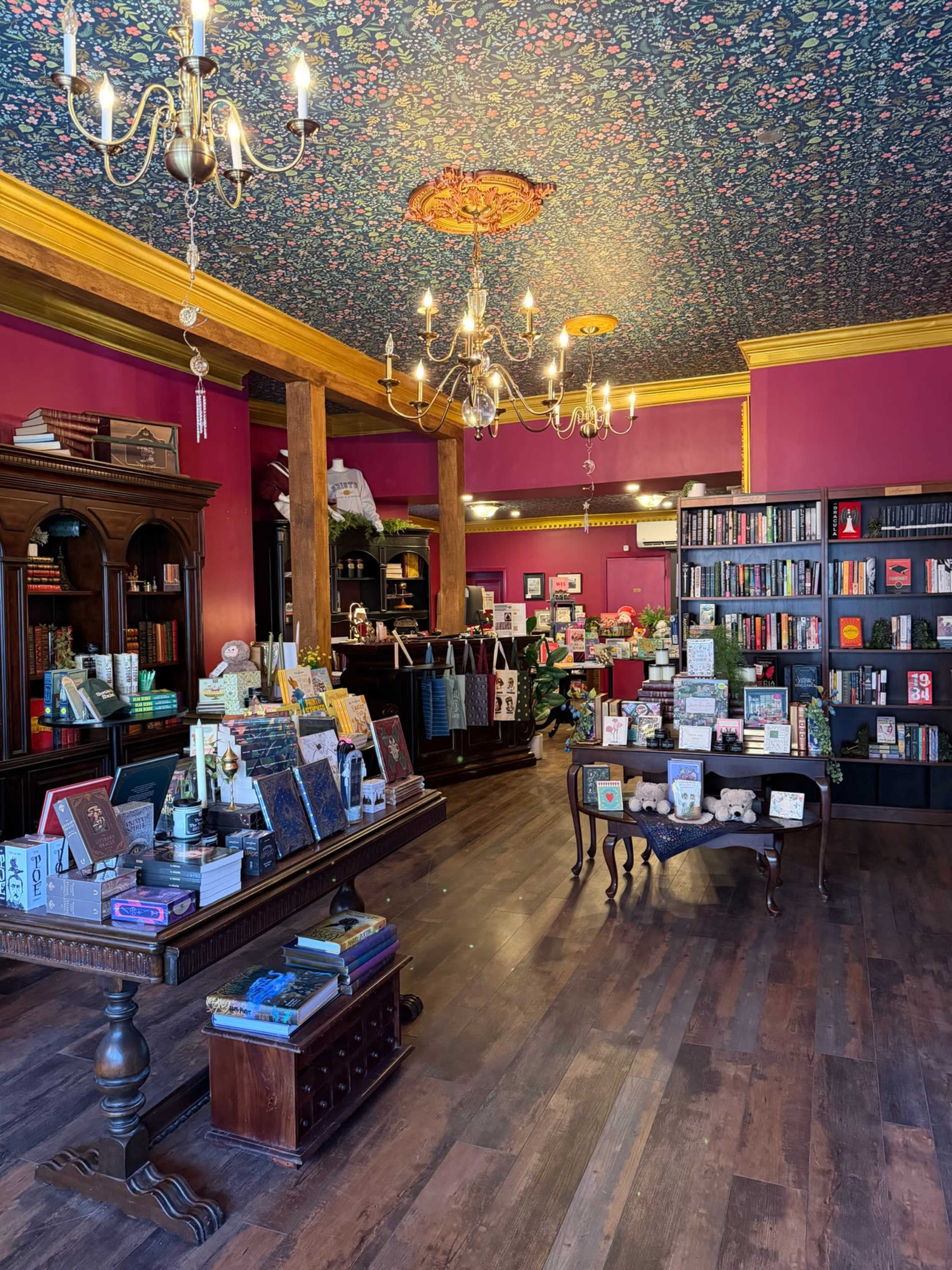 The image shows the interior of a colorful bookstore featuring wooden shelves filled with books, a decorative ceiling, and various displays of merchandise on tables.