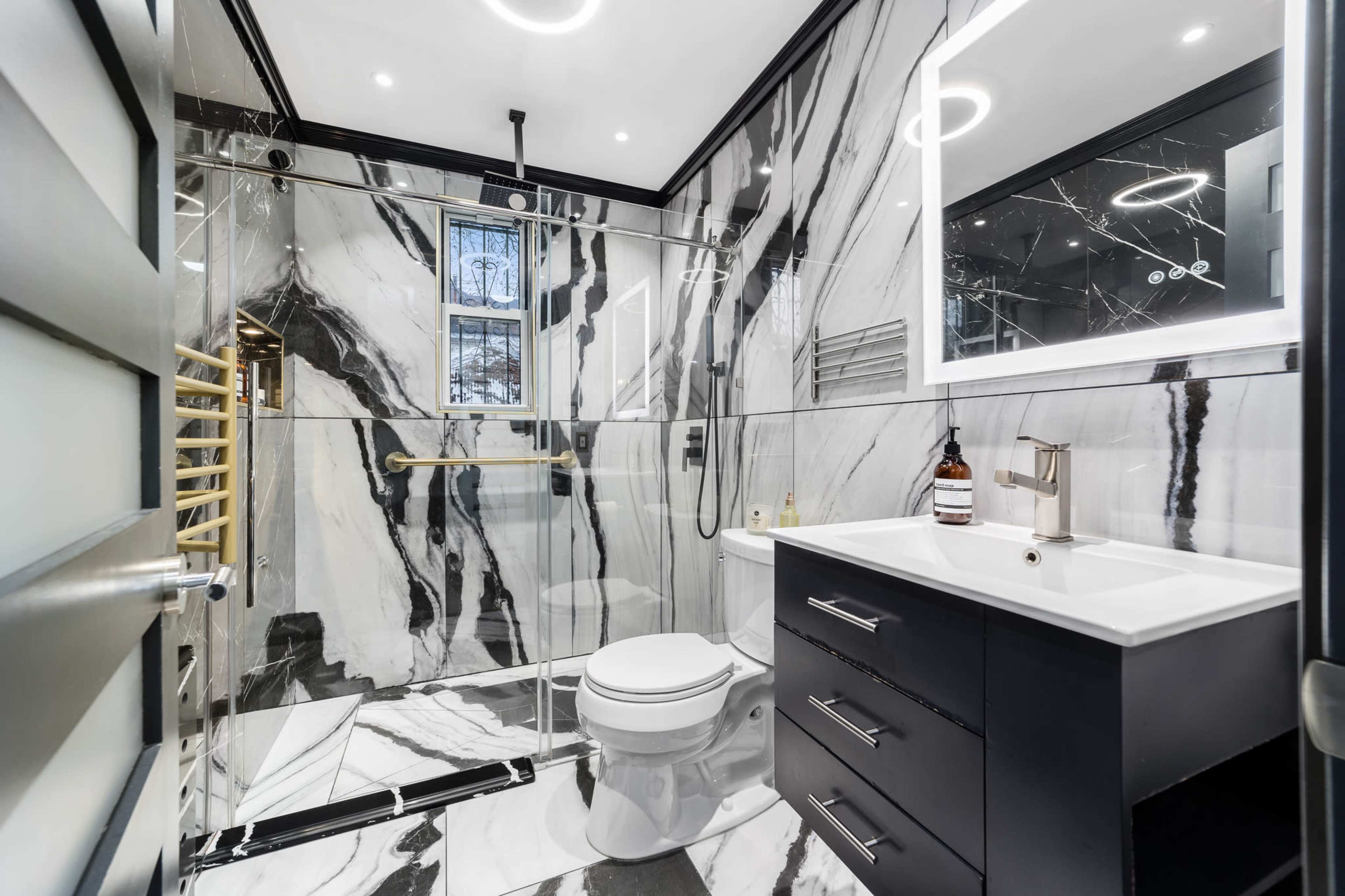 The bathroom features black and white marble walls, a glass shower enclosure, a modern vanity, and a sleek toilet.