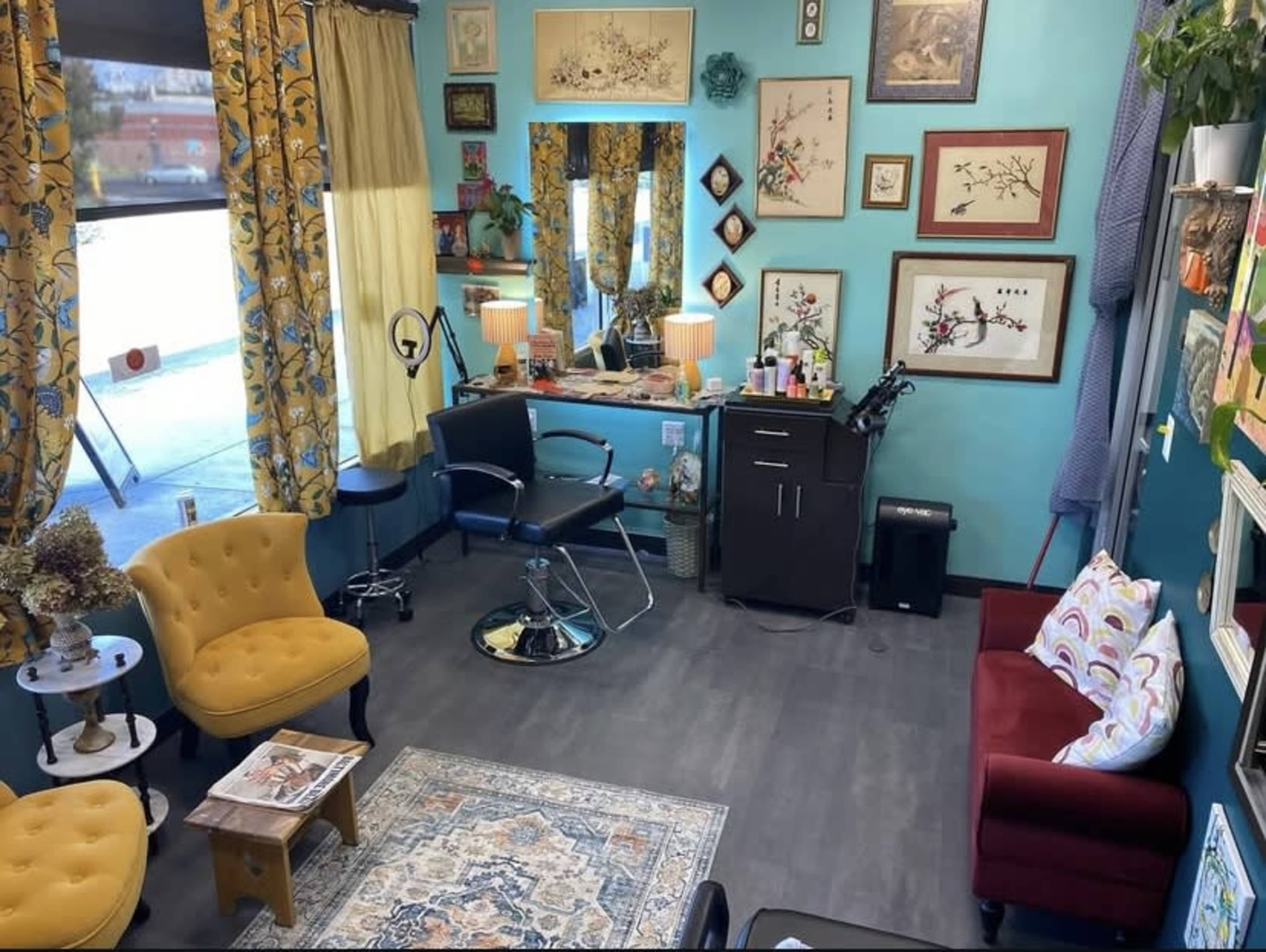 The image features a brightly colored salon interior with patterned curtains, various artworks on the walls, comfortable seating, and salon equipment arranged for client services.