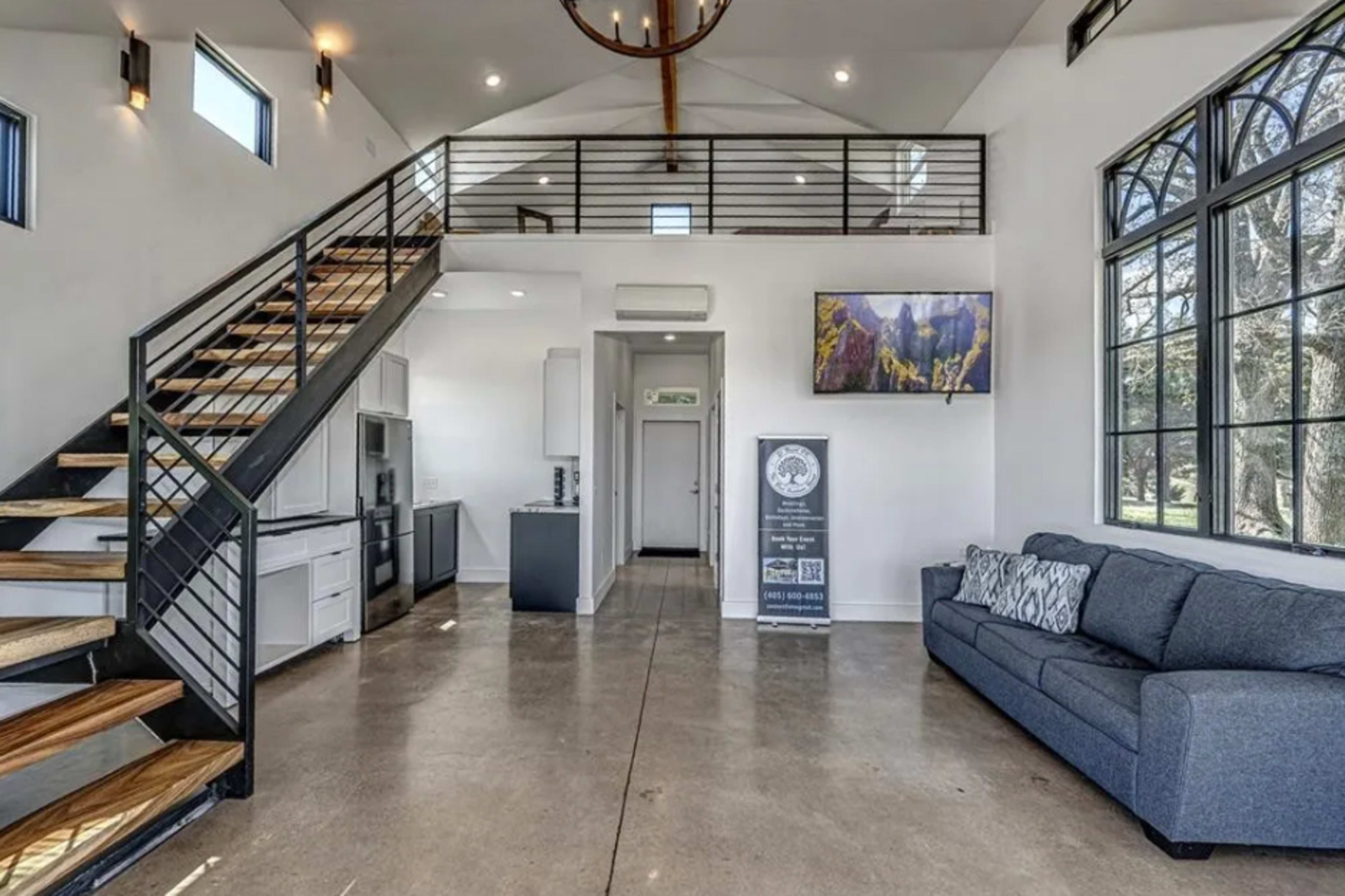 The interior of a modern living space features a staircase, an open kitchen area, and large windows that allow natural light to fill the room.