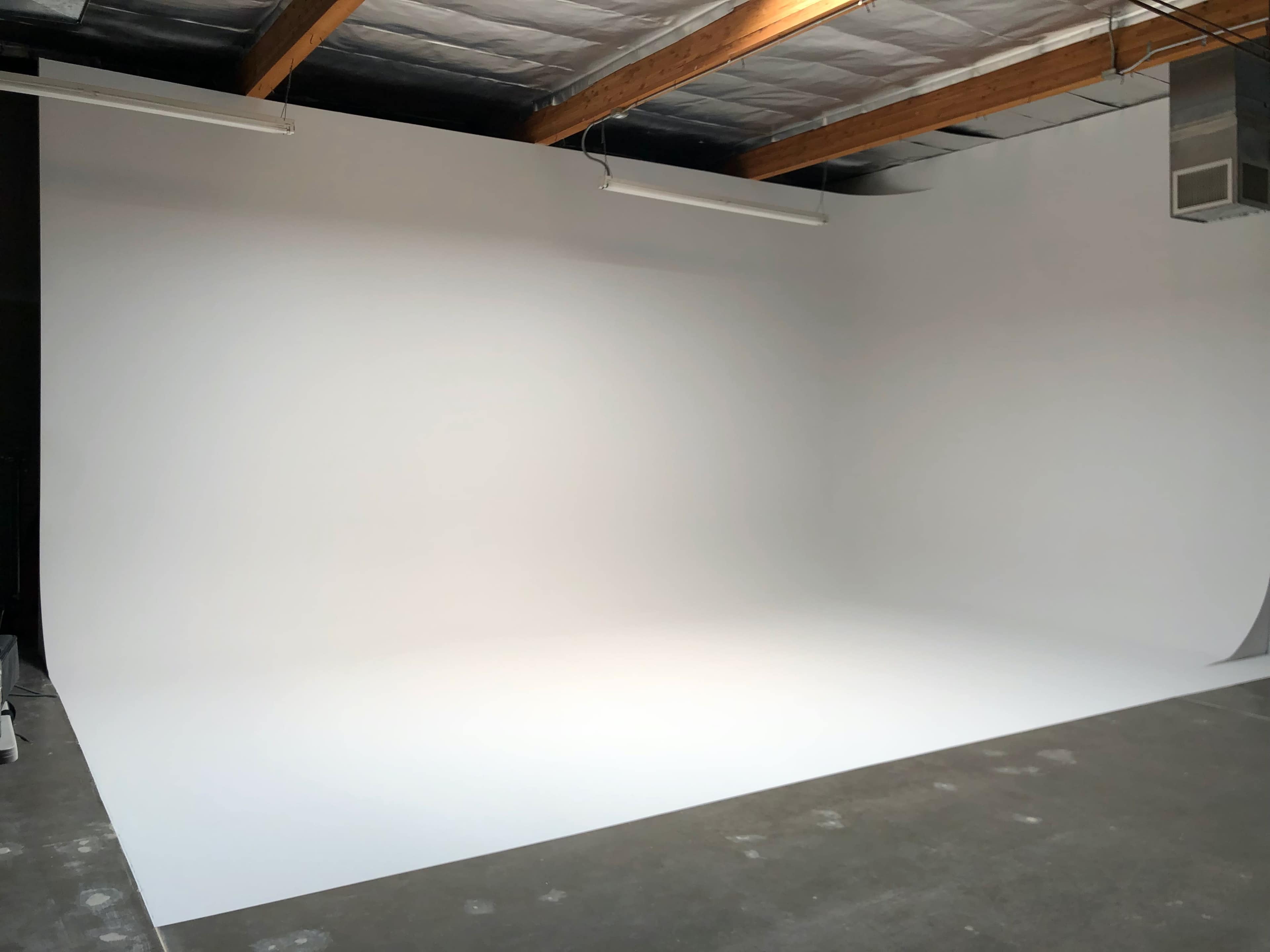 A spacious photography studio with a large, seamless white backdrop and exposed wooden beams on the ceiling.