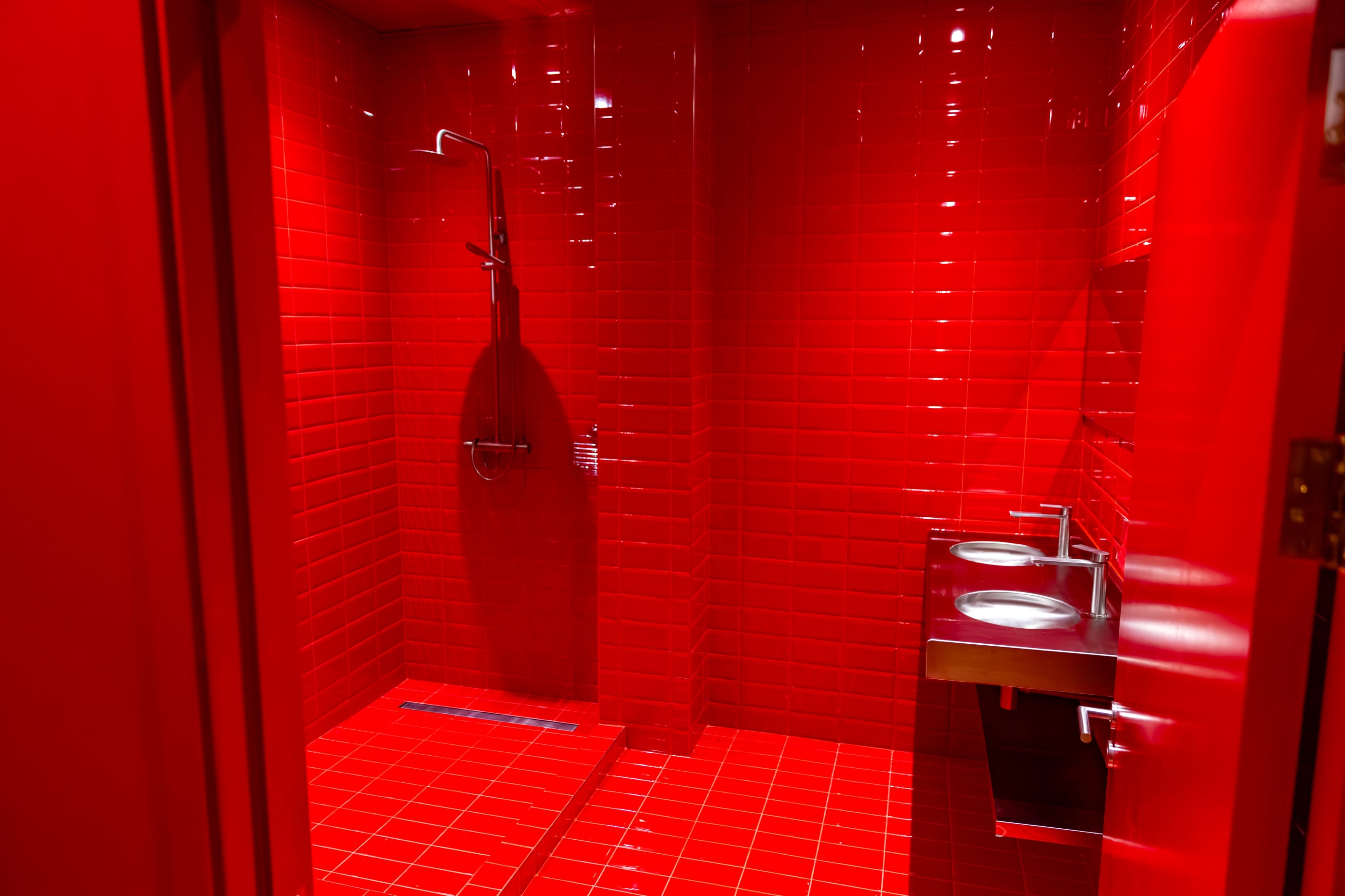 The image shows a restroom with bright red tiled walls and floors, featuring a shower area on one side and two sinks on the other.
