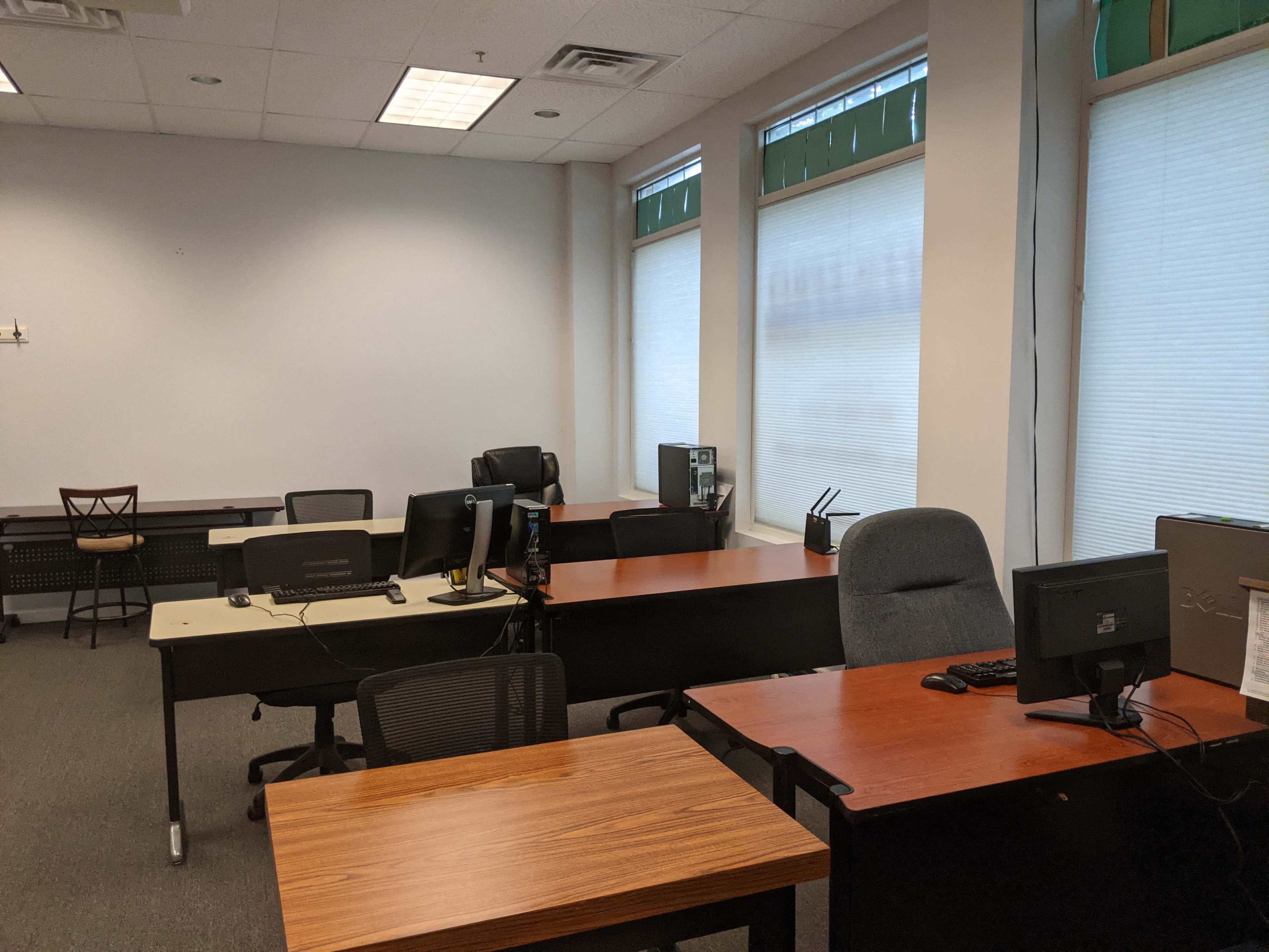 An office space with several desks and chairs arranged in a well-lit room with large windows.