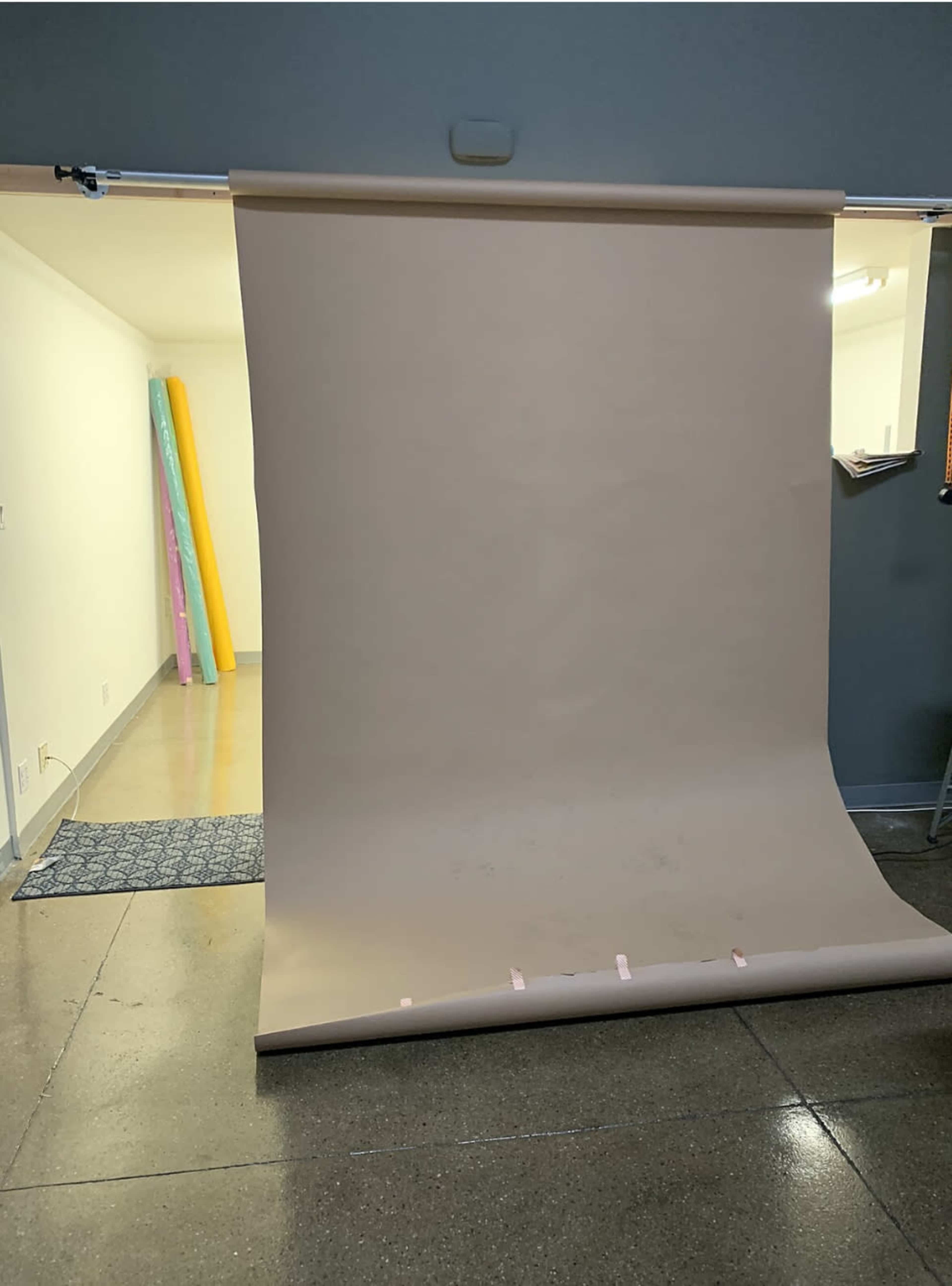 The image shows a large roll of seamless beige backdrop paper set up in a studio space with exposed walls and a tiled floor.