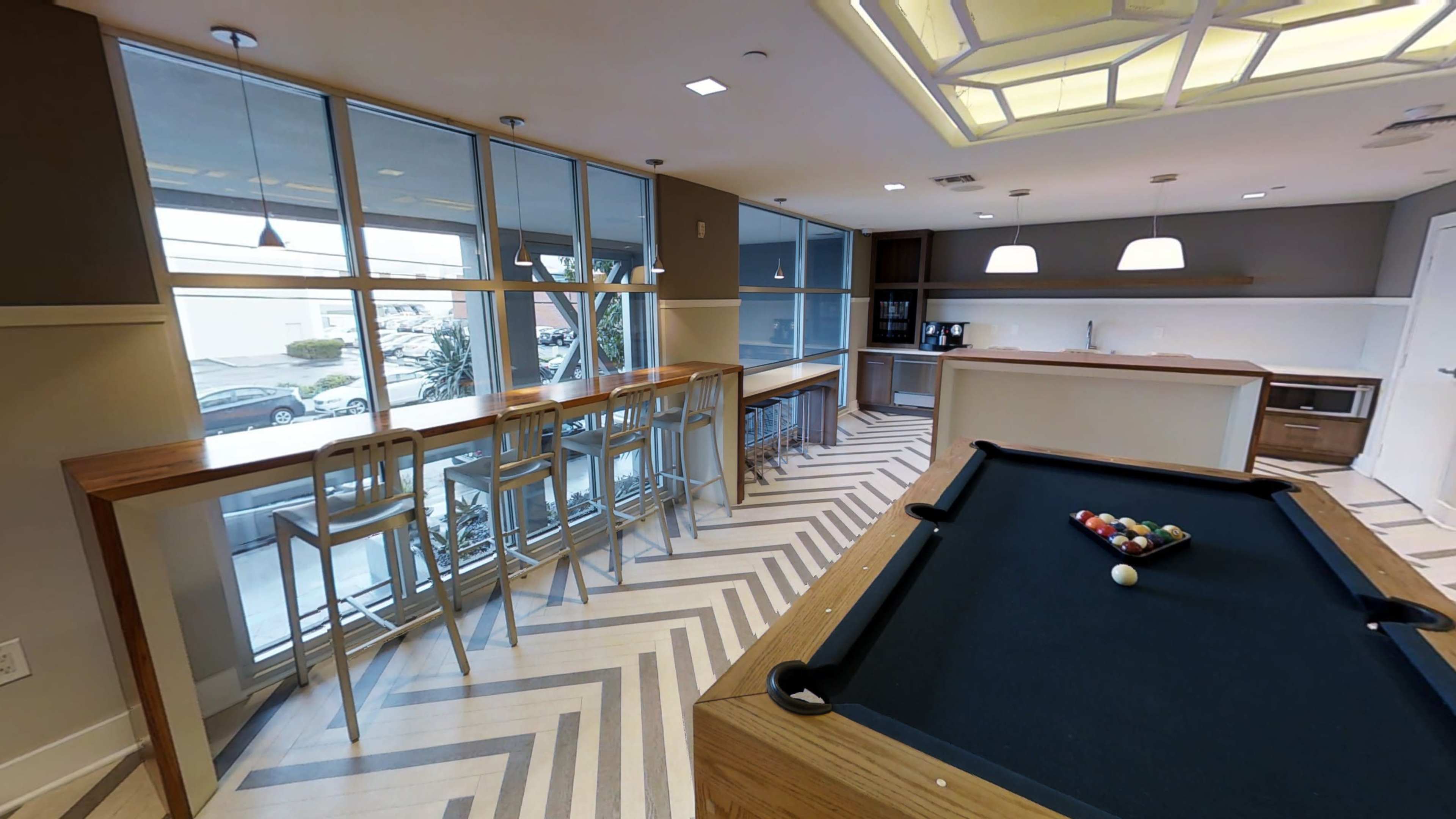 A modern game room with a pool table, high stools, and large windows.