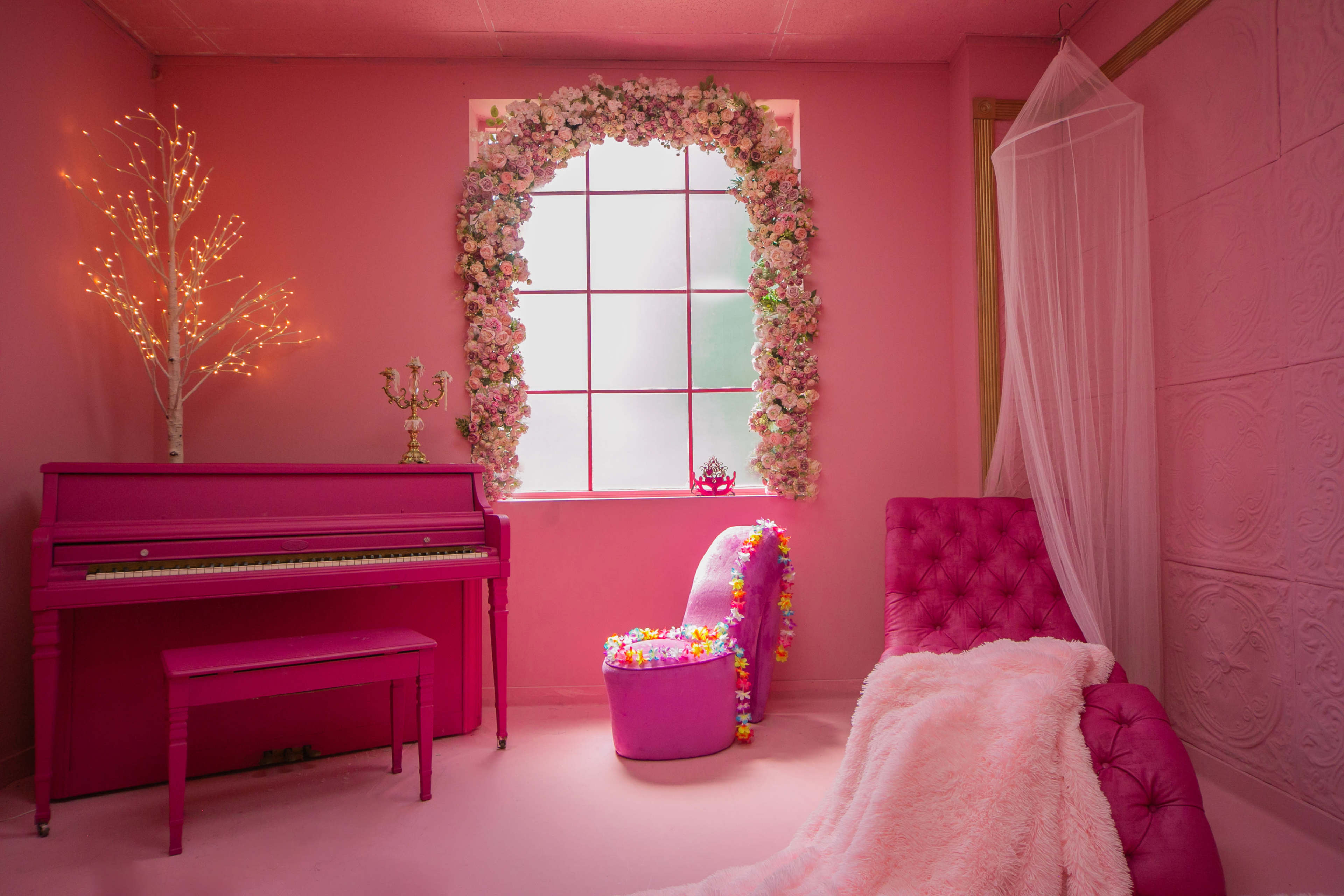 A pink-themed room featuring a pink piano, a chair adorned with flowers, and a window framed with floral decorations.