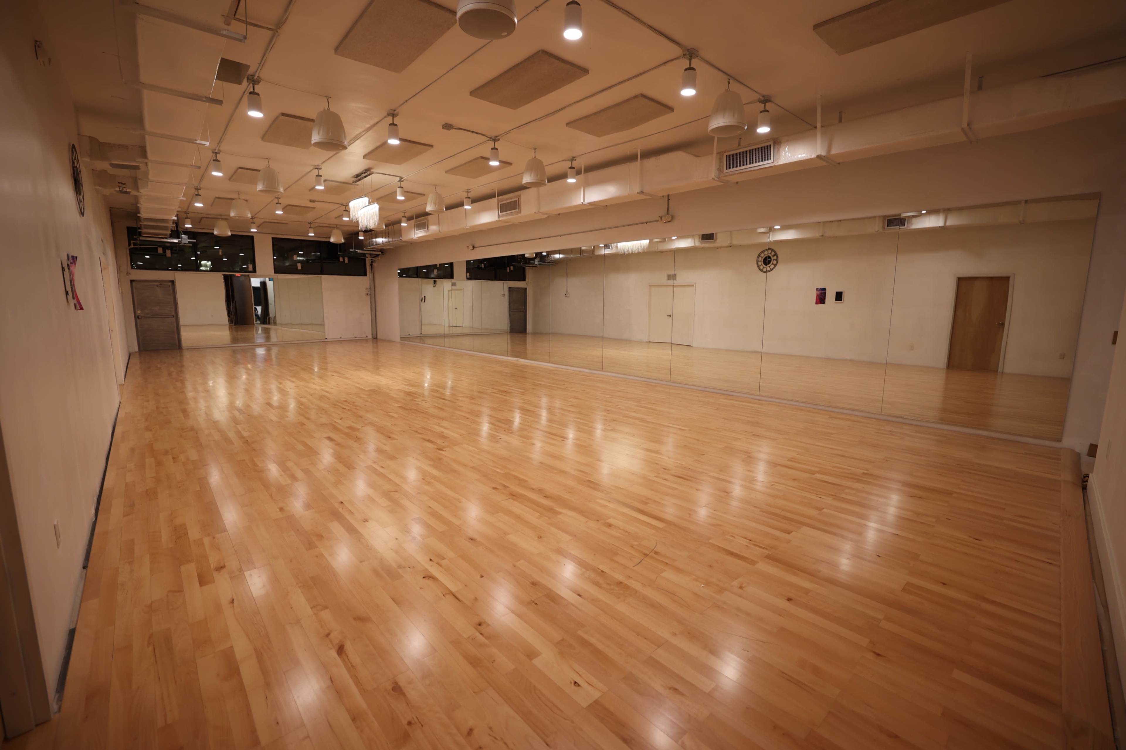 The image shows a spacious, well-lit studio with polished wooden floors and large mirrors along one wall.