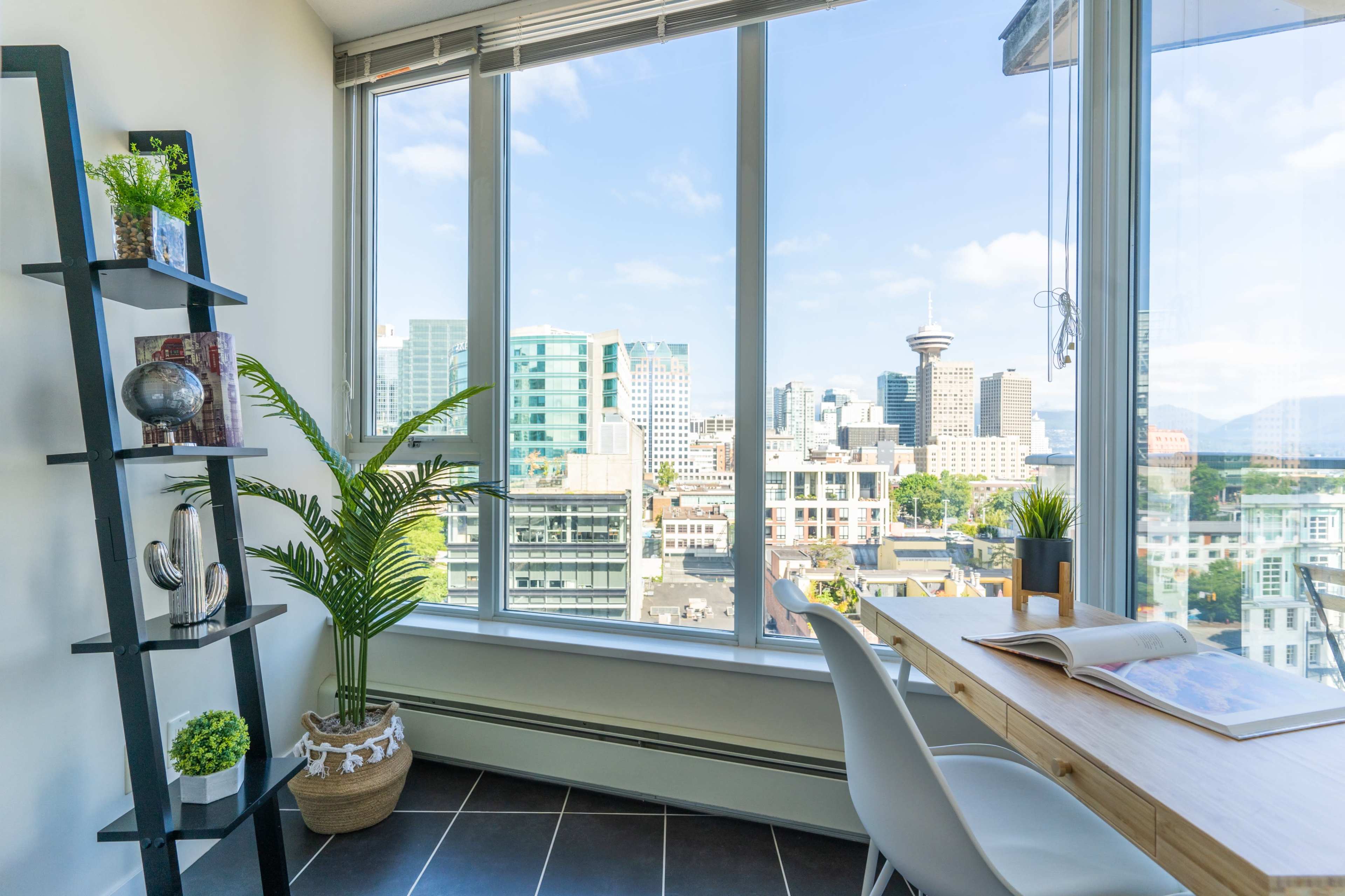 A modern workspace features a wooden desk beside a large window displaying a city skyline with tall buildings.