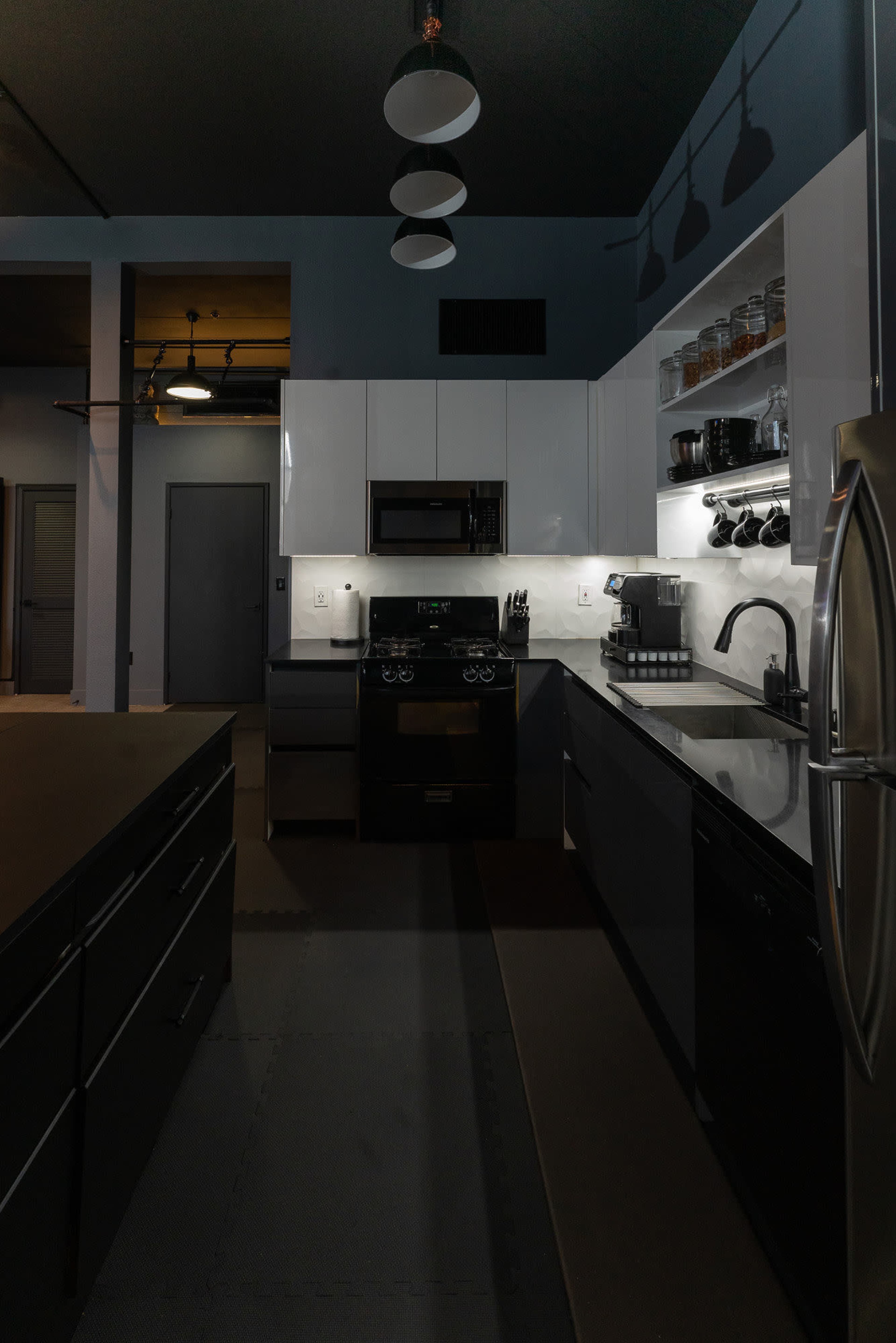 A modern kitchen features sleek black and white cabinetry, stainless steel appliances, and overhead pendant lighting.
