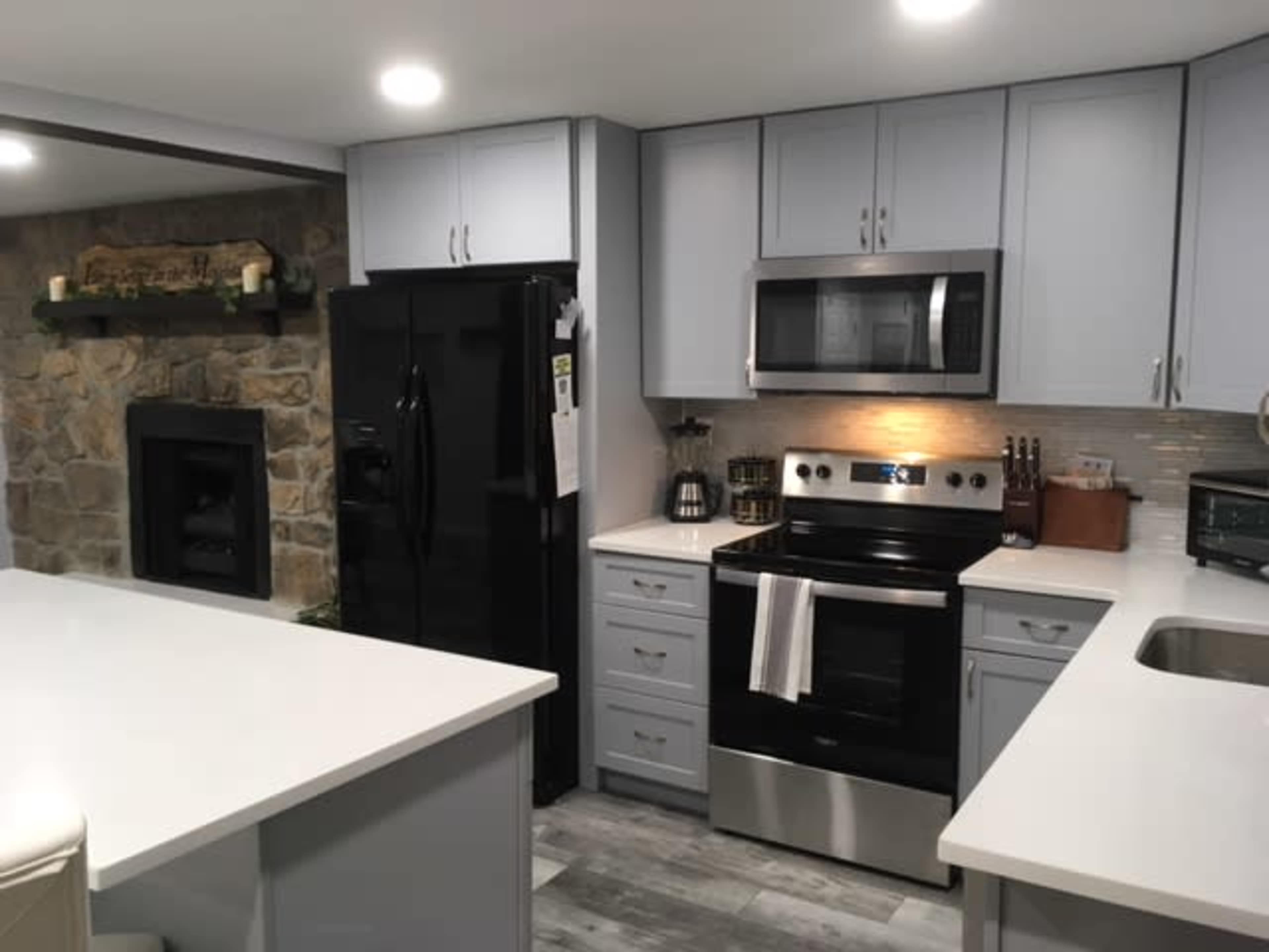 A modern kitchen featuring gray cabinetry, a black refrigerator, and a stainless steel oven and microwave.