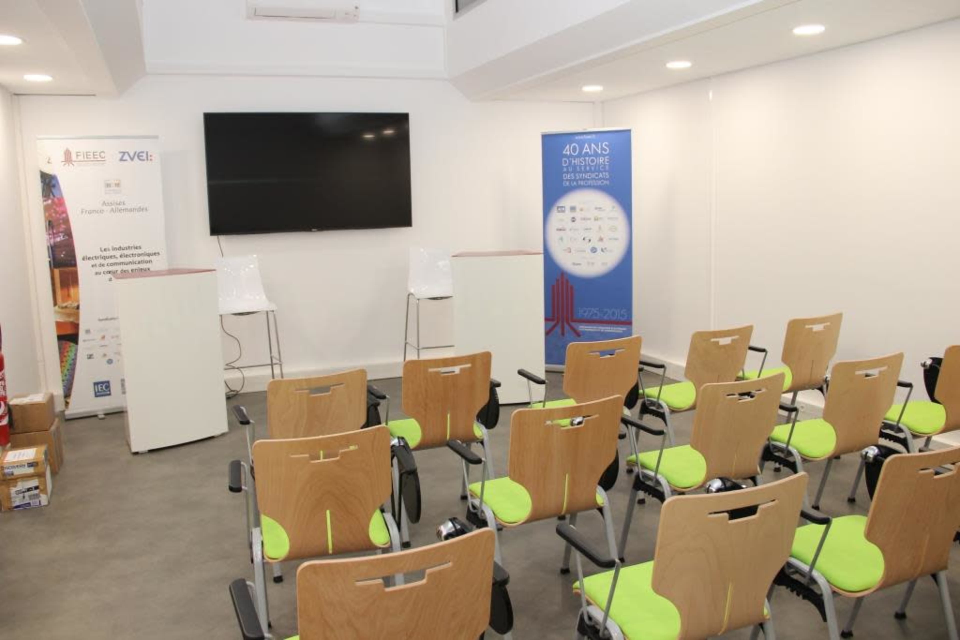 An empty conference room is set up with rows of chairs and a large screen, featuring a banner celebrating an anniversary.