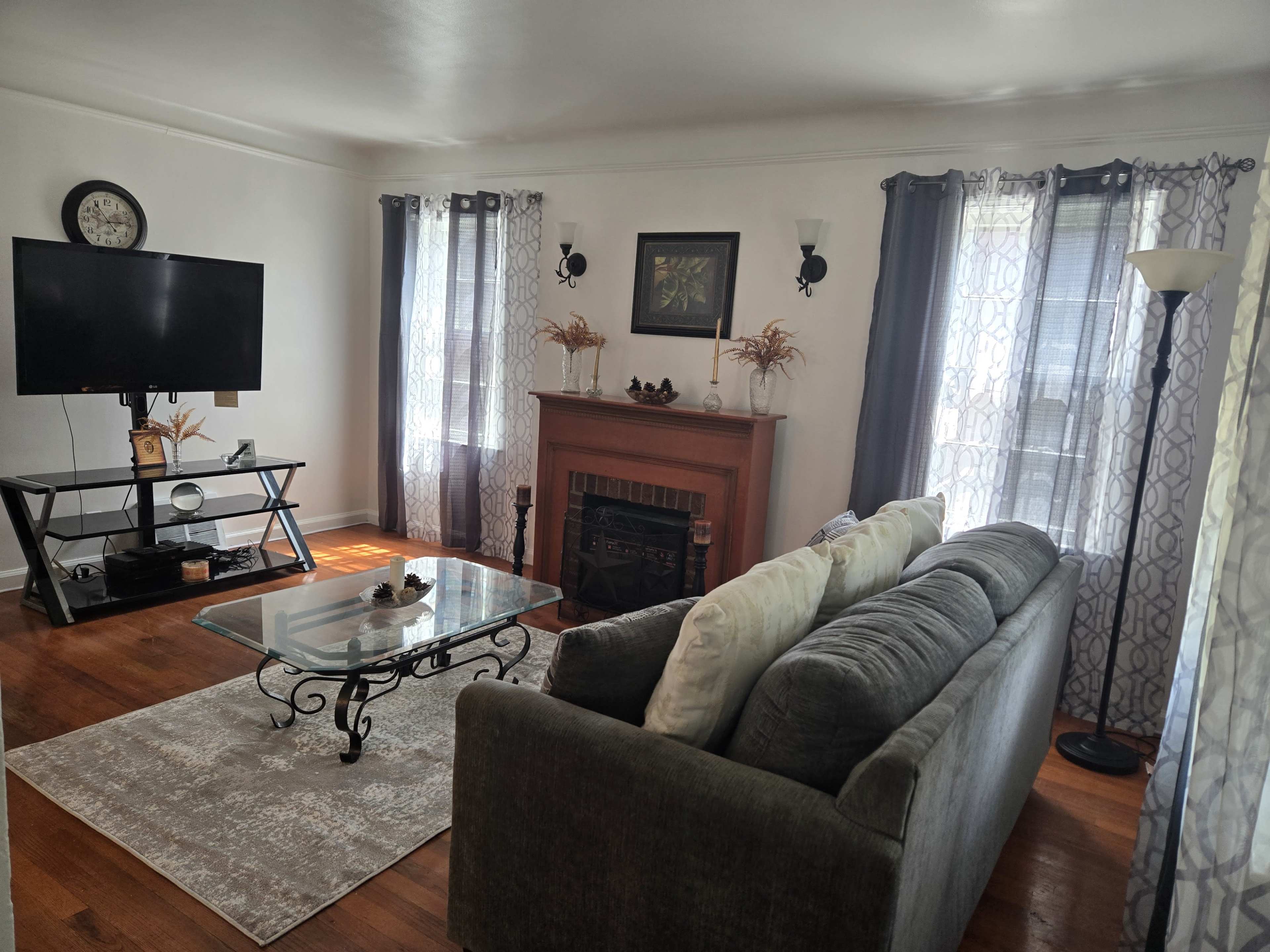 The living room features a gray sofa, a glass coffee table, a wooden fireplace, and a large flat-screen television on a stand.