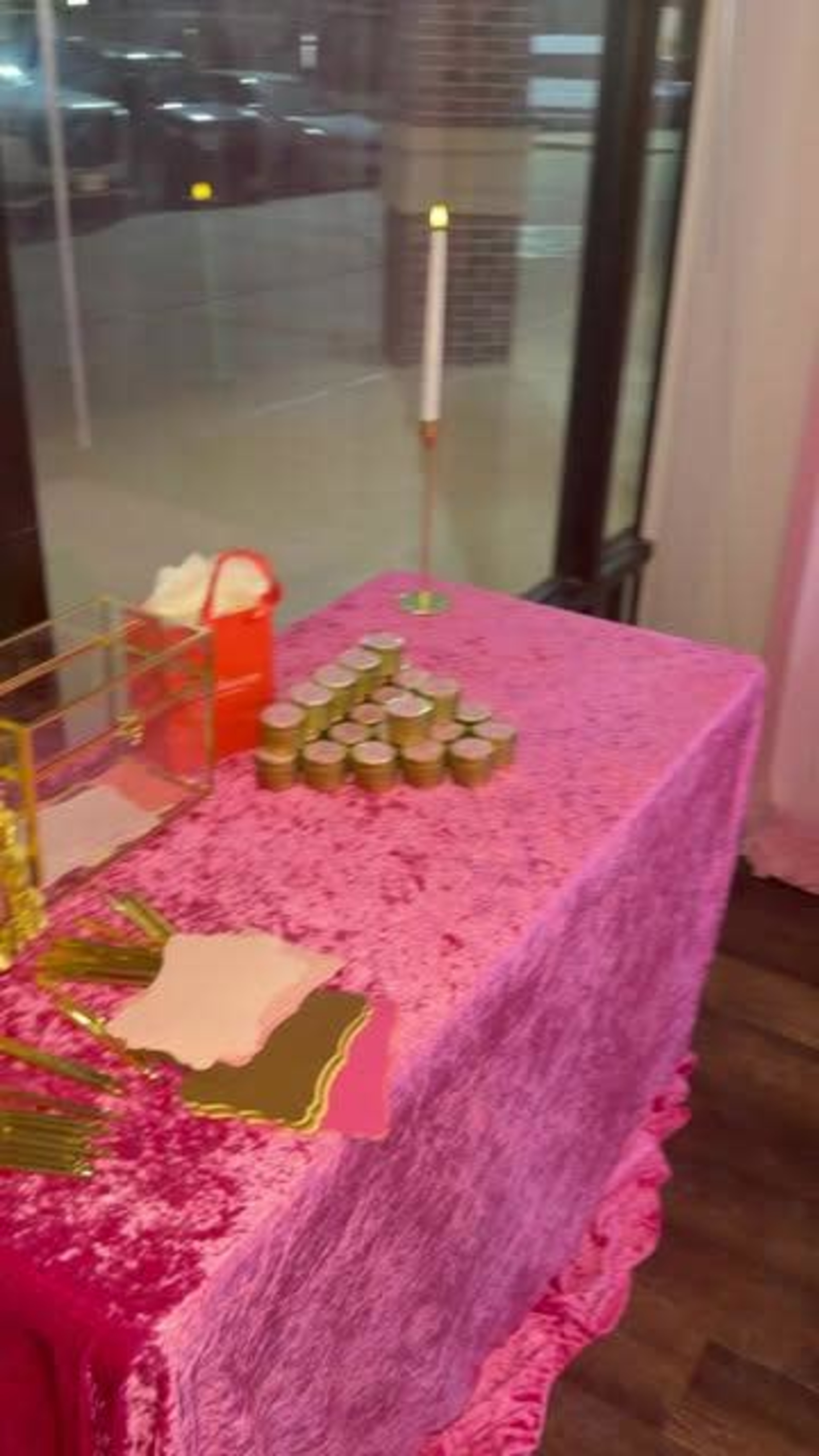 A table with a pink tablecloth displays jars arranged in a row, along with a lit candle and decorative items.