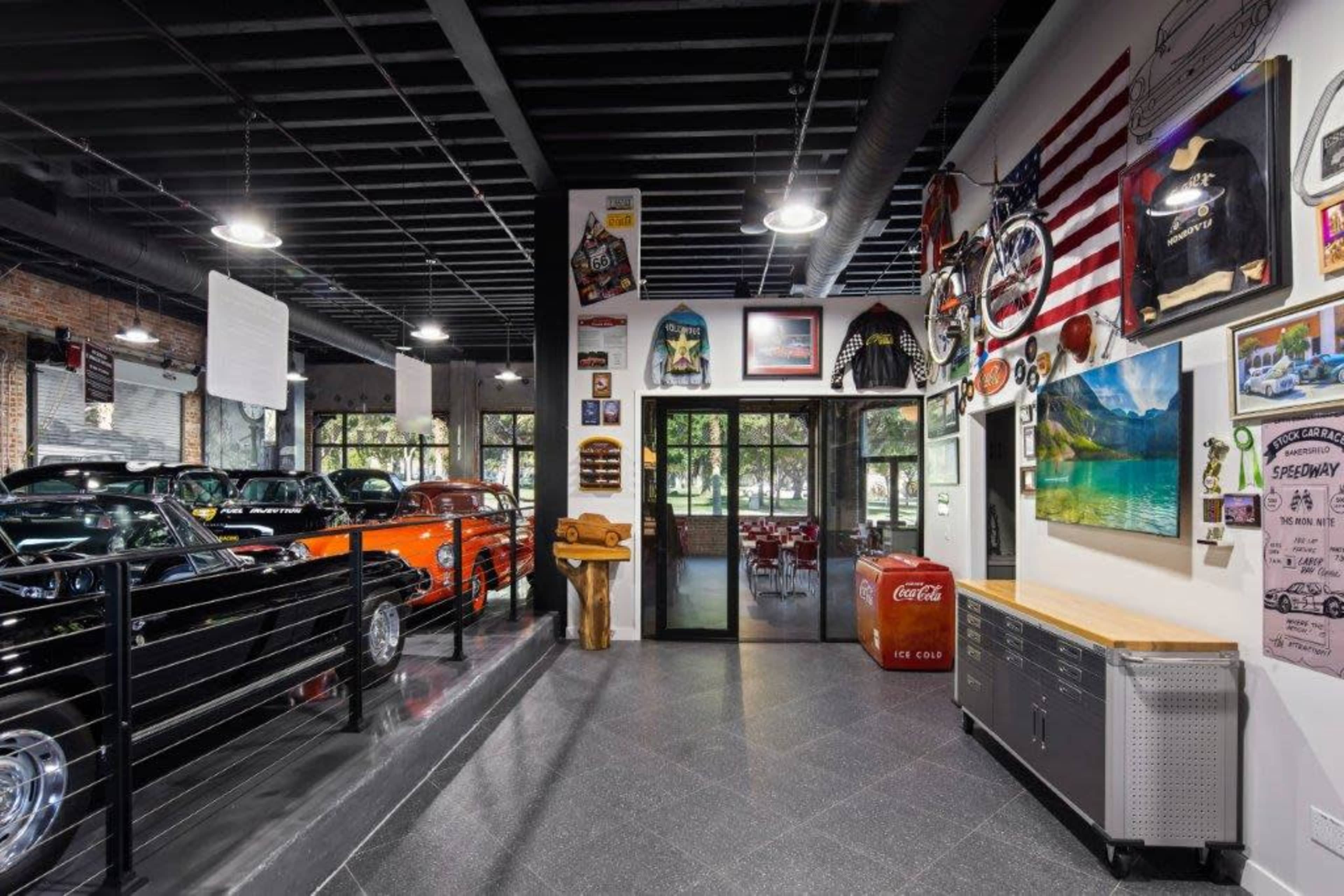 A well-organized car showroom featuring classic cars, decorative memorabilia, and a large glass entrance leading to a dining area.