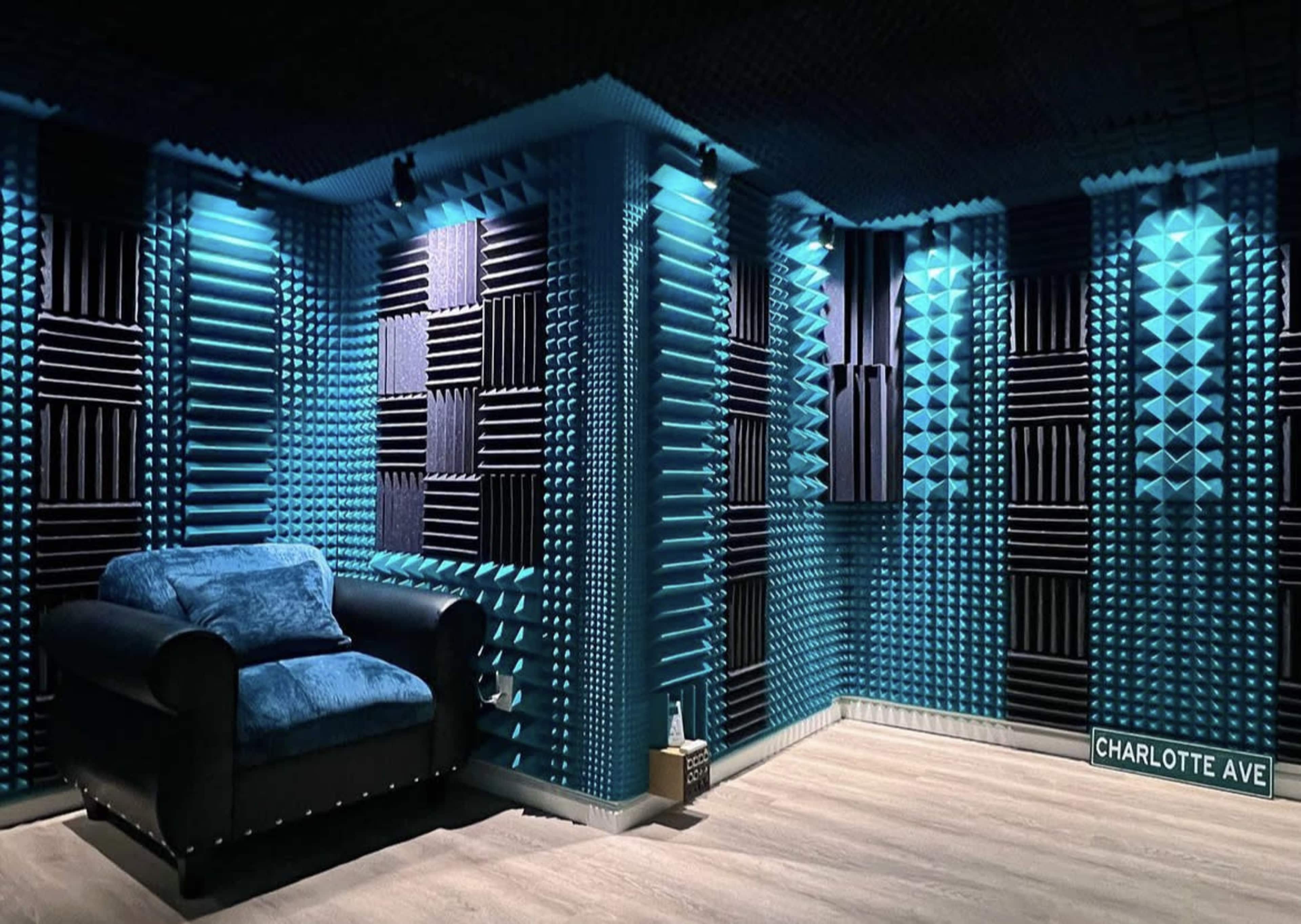 A soundproof room with blue acoustic panels on the walls and a dark blue armchair in one corner.