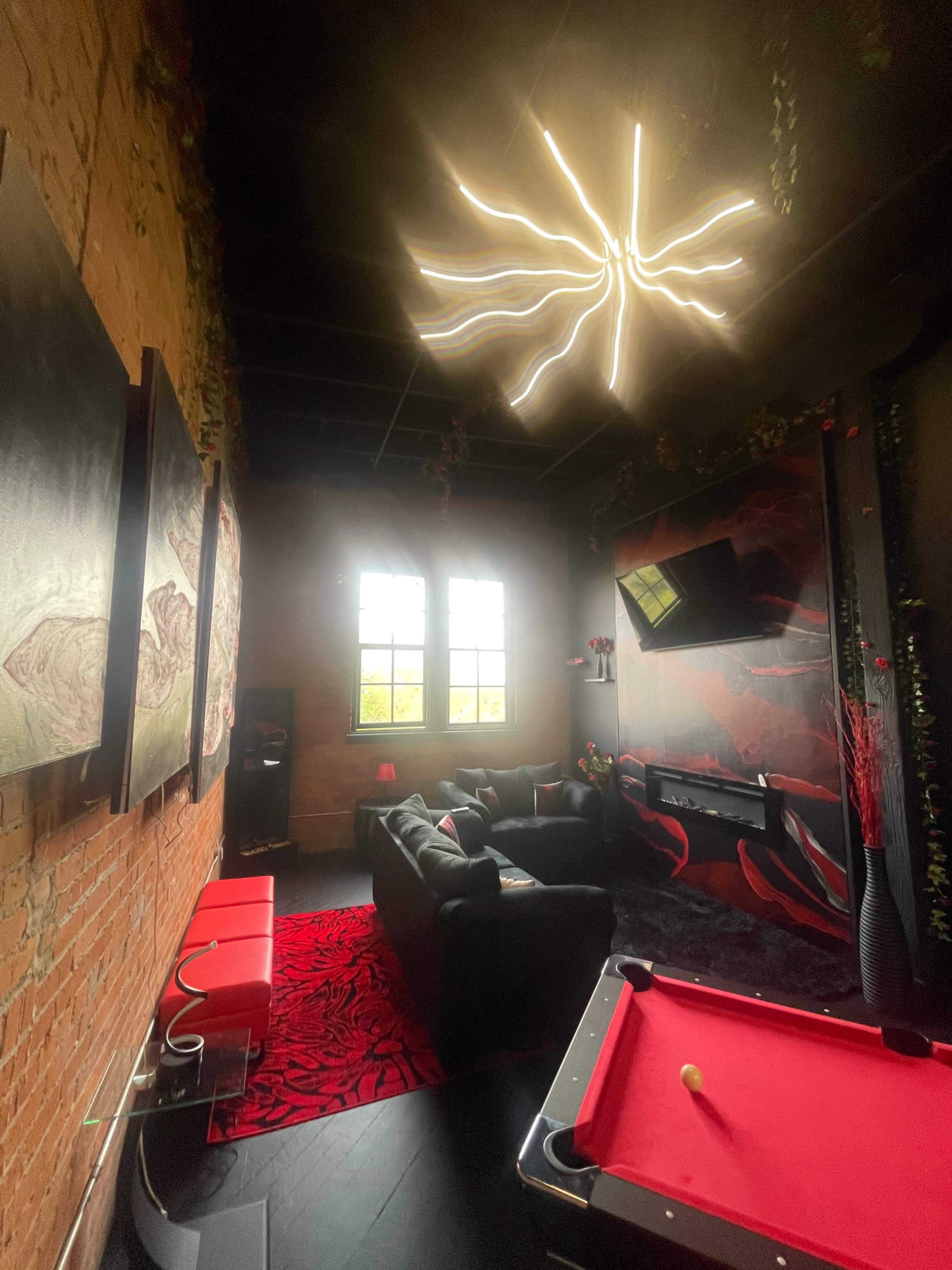 A cozy game room with a pool table, a black couch, and artistic wall decorations set against exposed brick.
