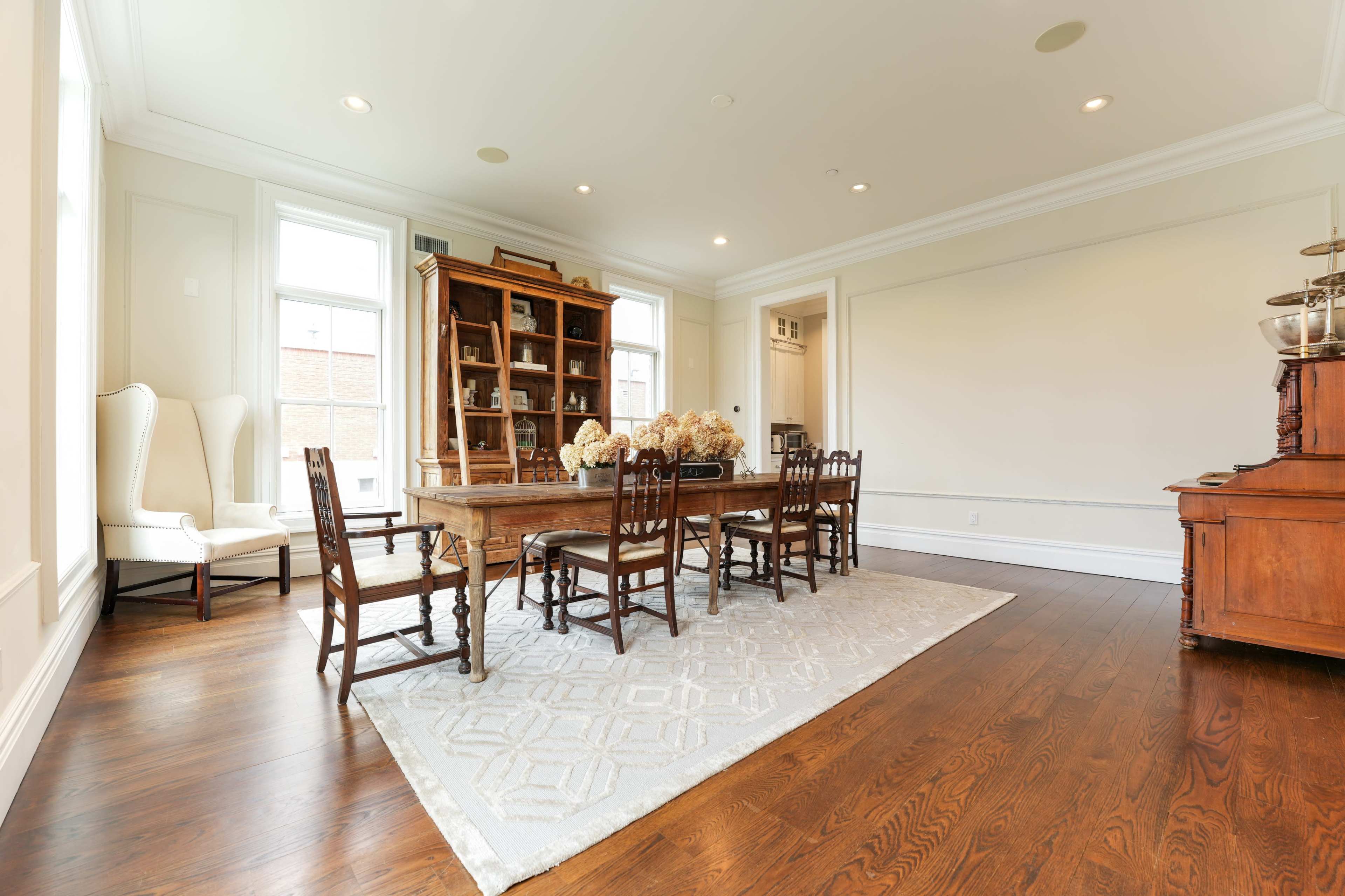 A spacious dining room featuring a long wooden table surrounded by chairs, with a china cabinet and upholstered chairs in the background.