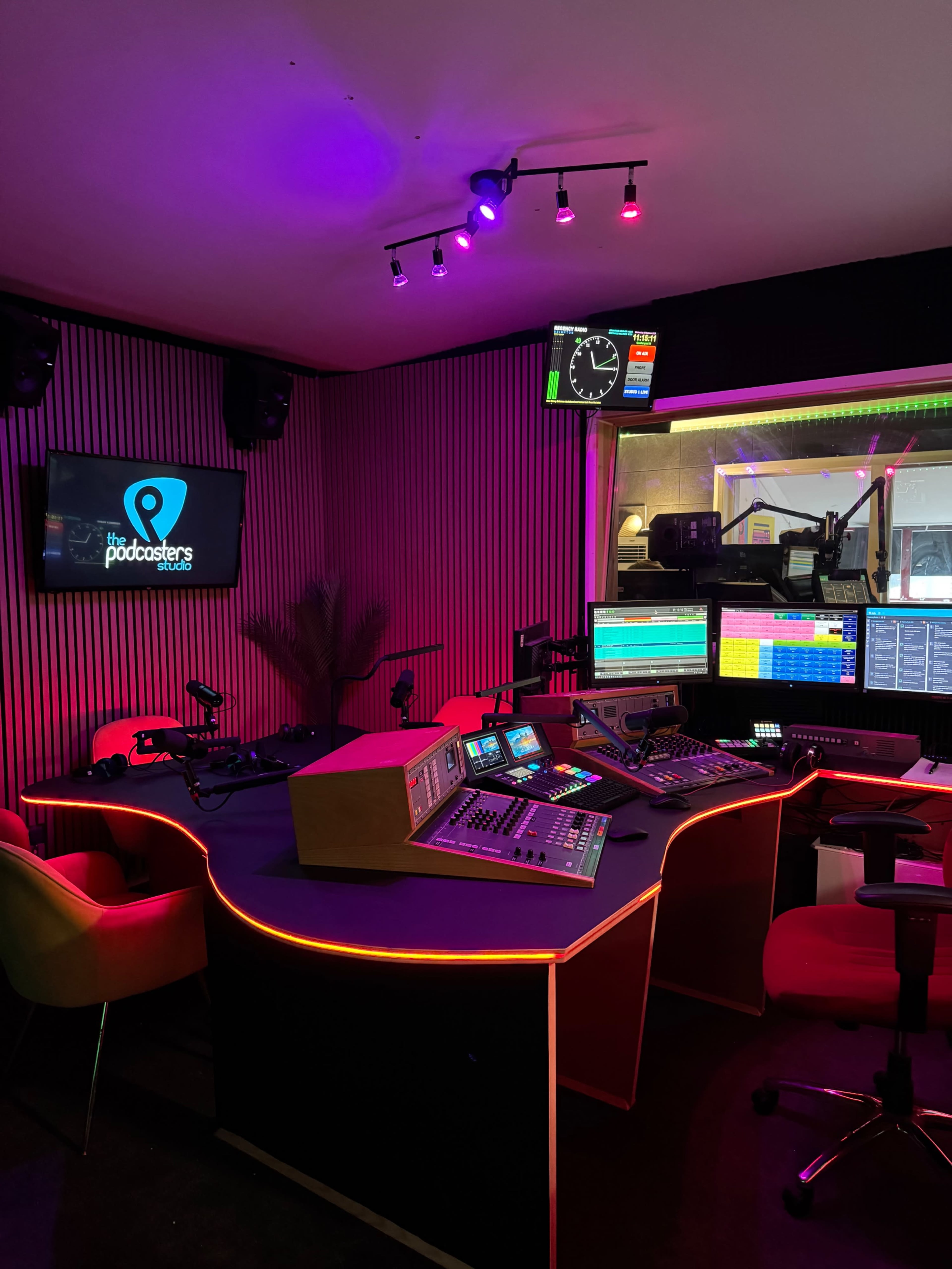The image shows a modern podcast studio featuring sound equipment, control panels, and colorful ambient lighting.